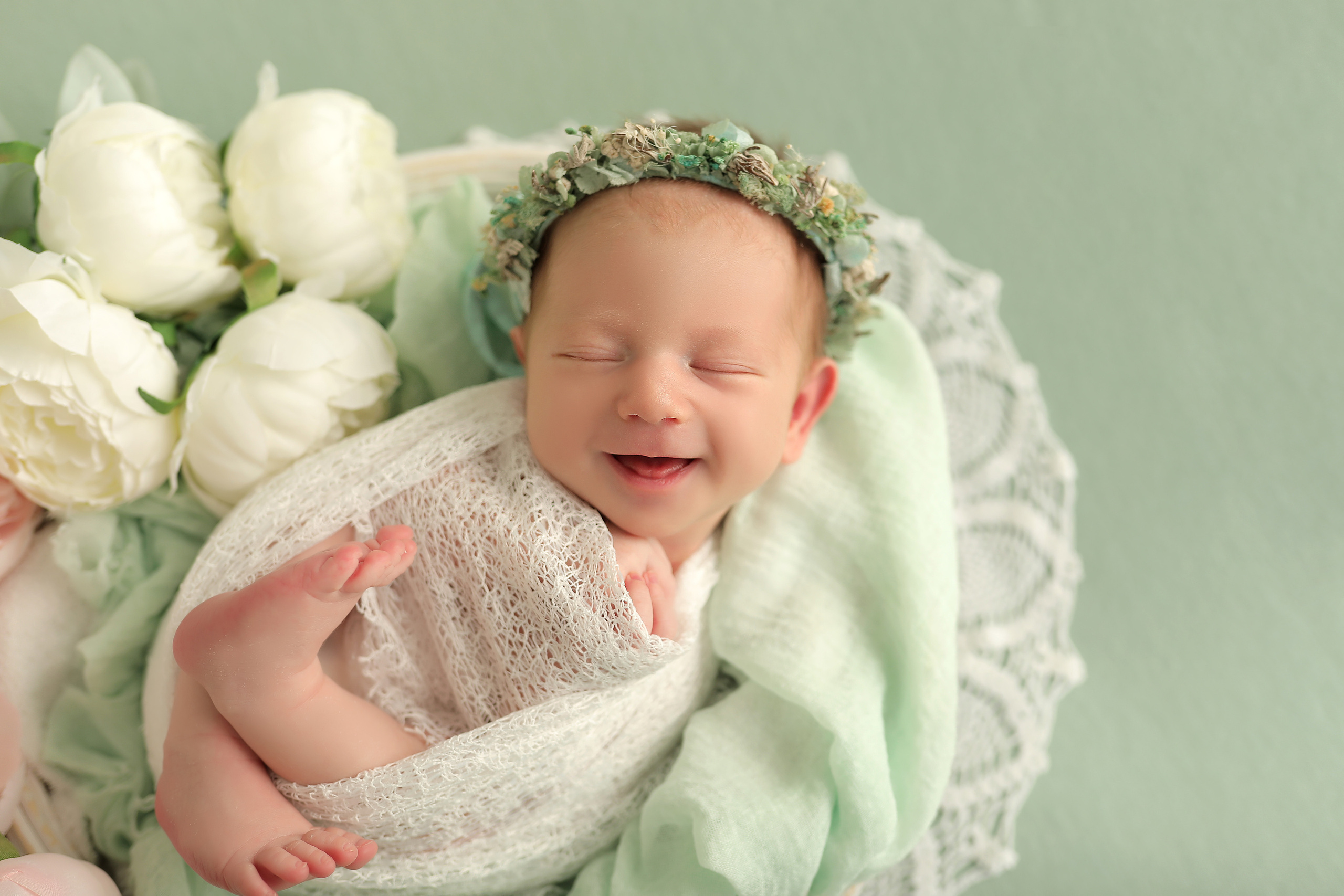 новорожденная девочка с улыбкой в мятной обмотке с цветами и веночком