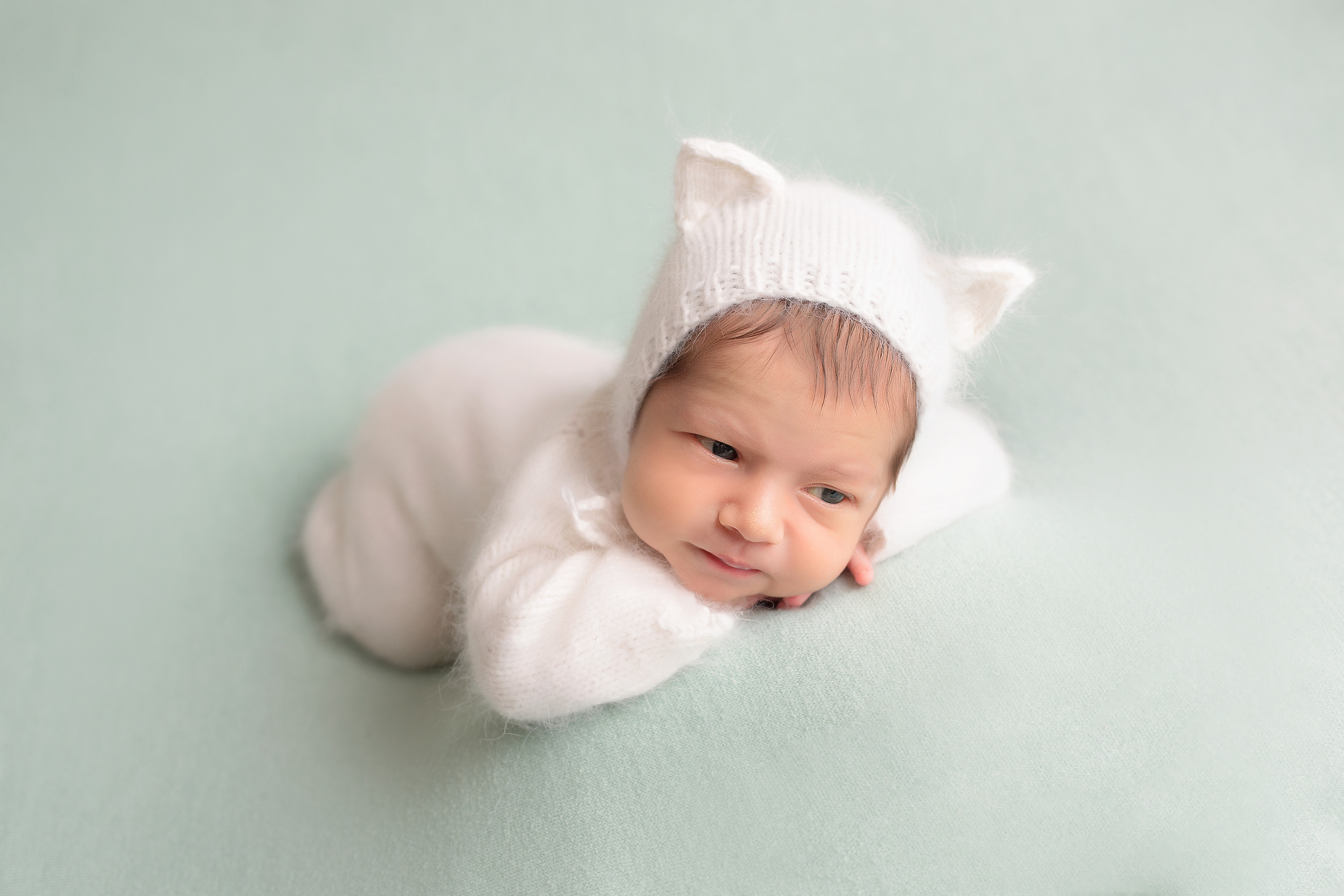 новорожденный в белом пушистом костюме и в шапочке котенка с ушками