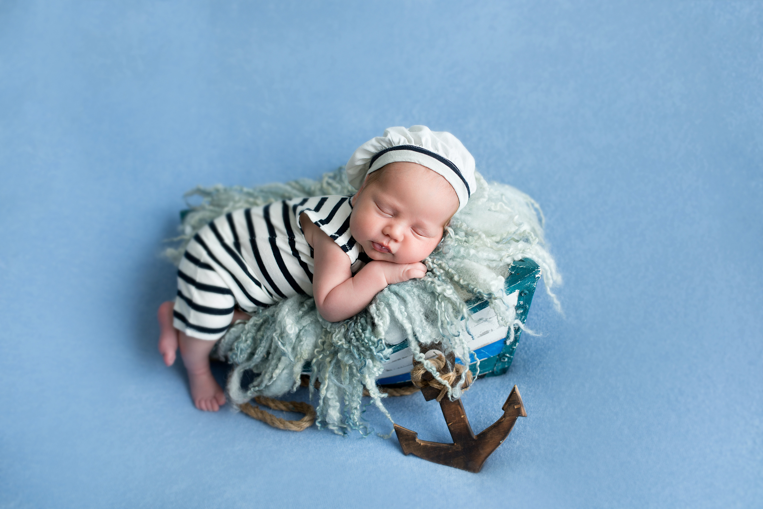 новорожденный мальчик в тельняшке в лодке с якорем на голубом фоне