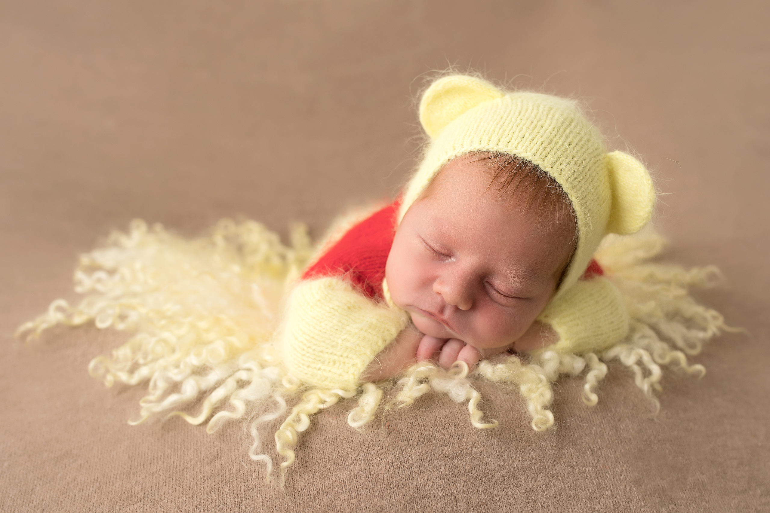 портрет новорожденного малыша в шапочке Винни-пуха на желтом пушистом коврике