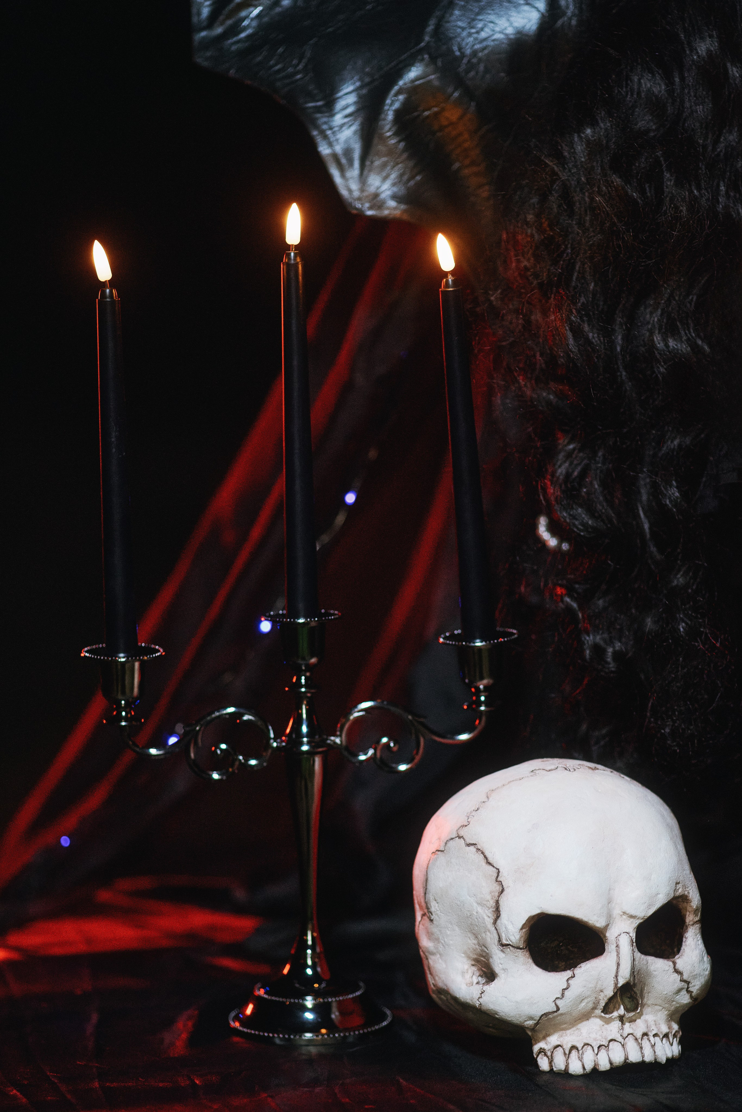 Человеческий череп, подсвечник с тремя свечами и чёрная ткань с красной подсветкой