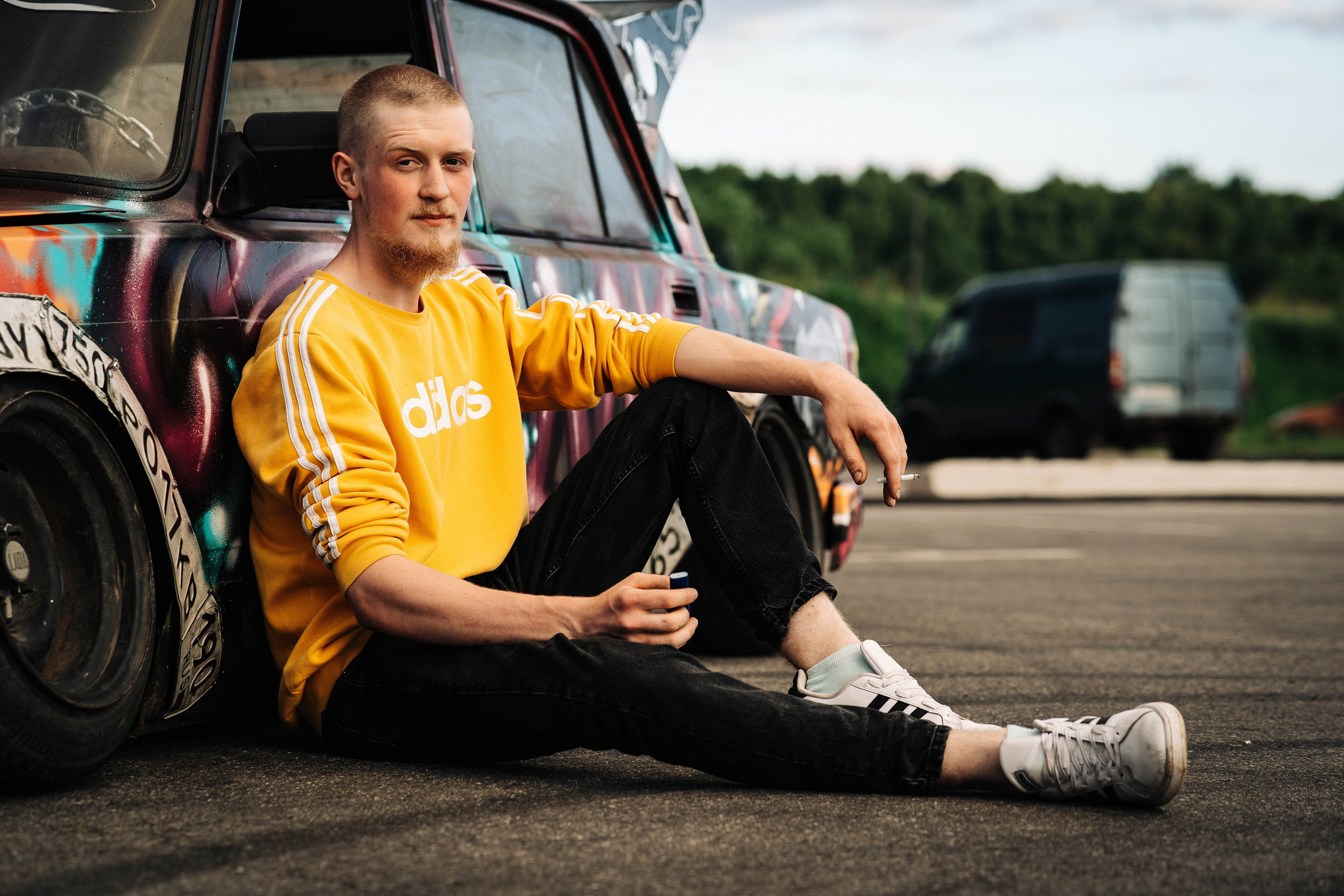 парень в желтой футболке сидит на асфальте прижавшись спиной к старому автомобилю