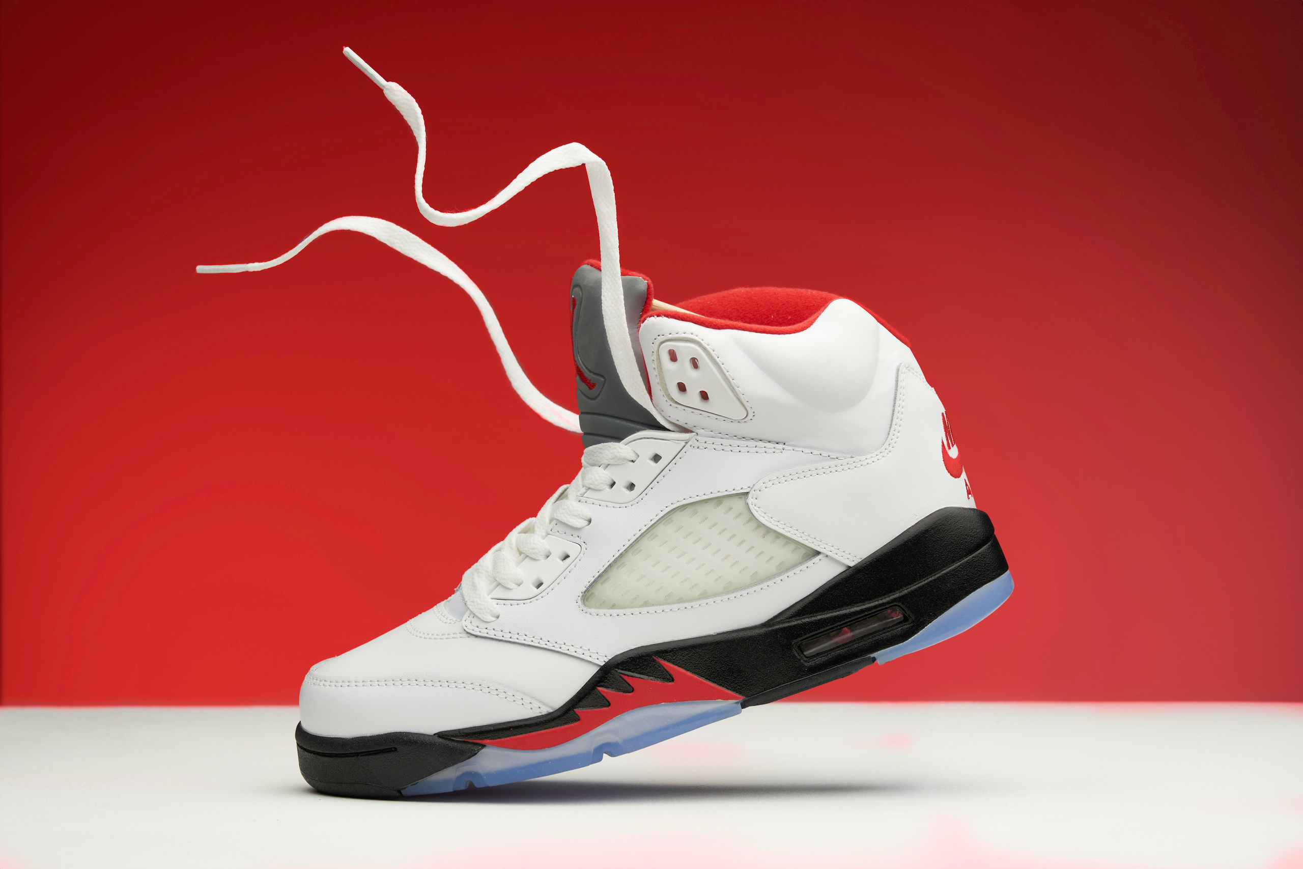 кросовок белый с парящими шнурками стоит носком на белом столе