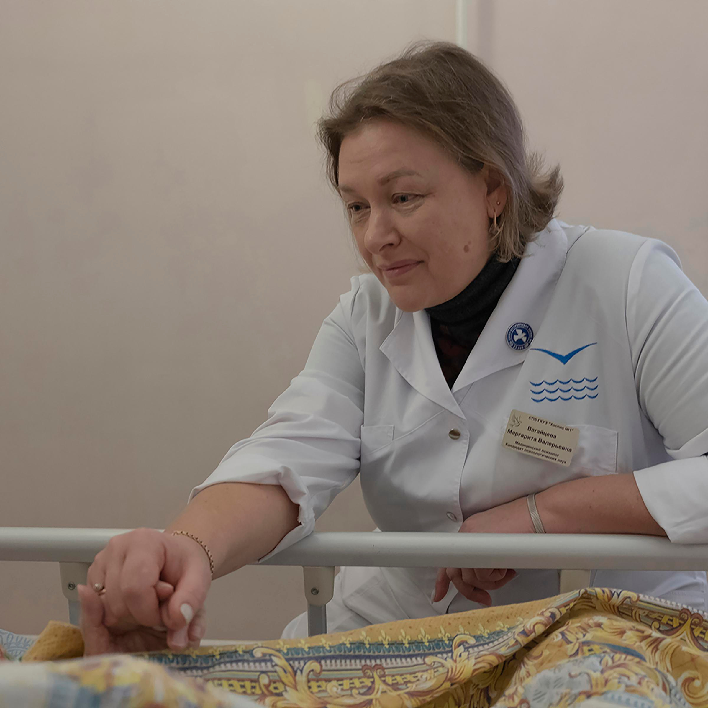 Psychologist in St. Petersburg Hospice is sitting near her mother’s bed and holding her arm. Her mother passed away few days later.