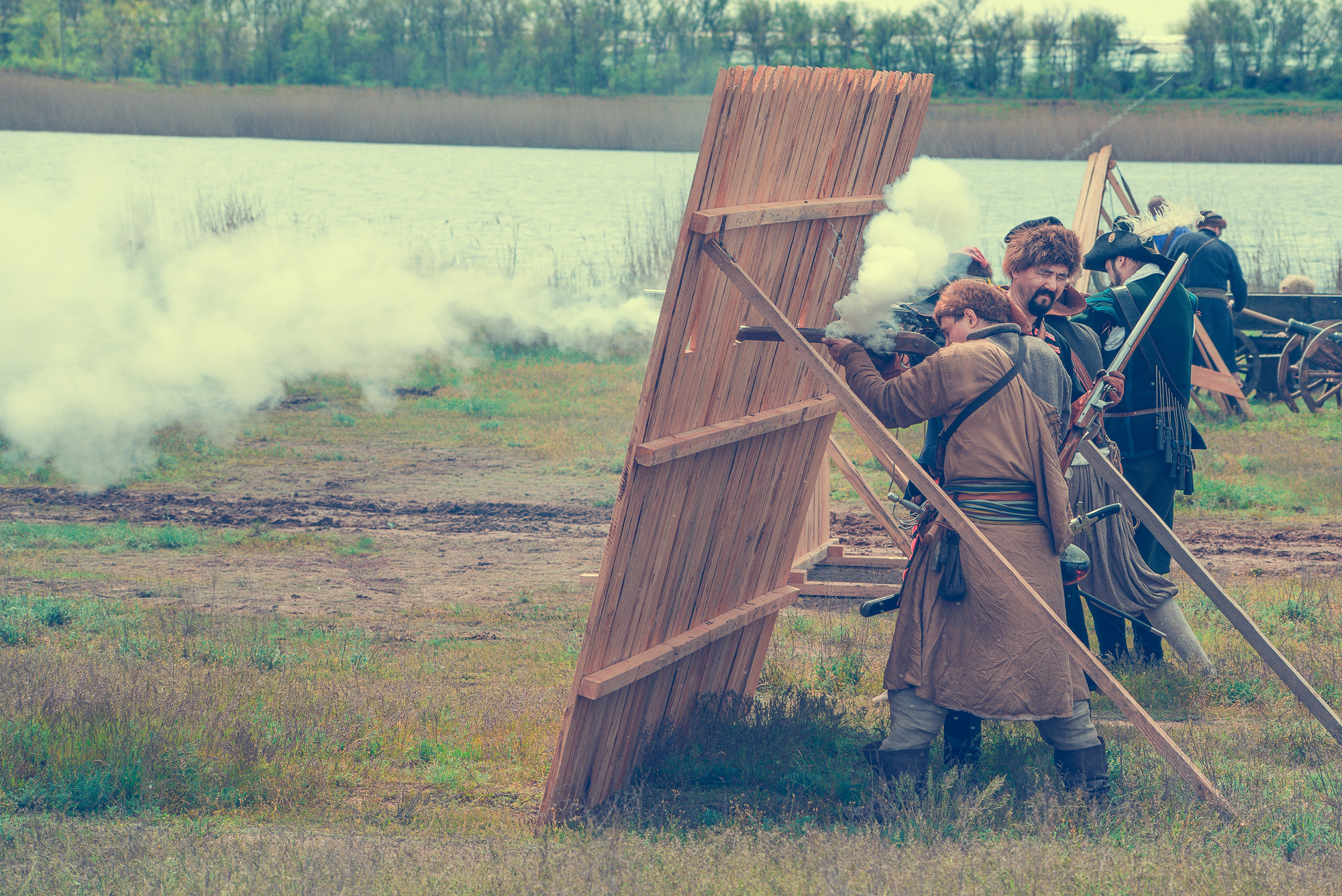 Атакующие стреляют из старинных оружий из-за деревянного ограждения