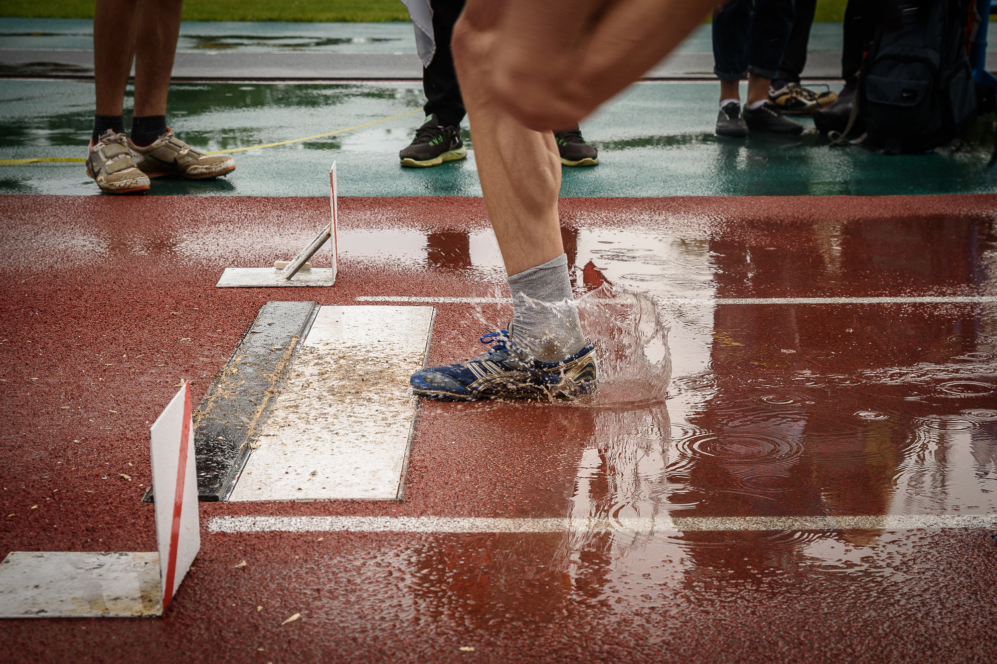 Нога спортсмена поднимает брызги из лужи перед тройным прыжком