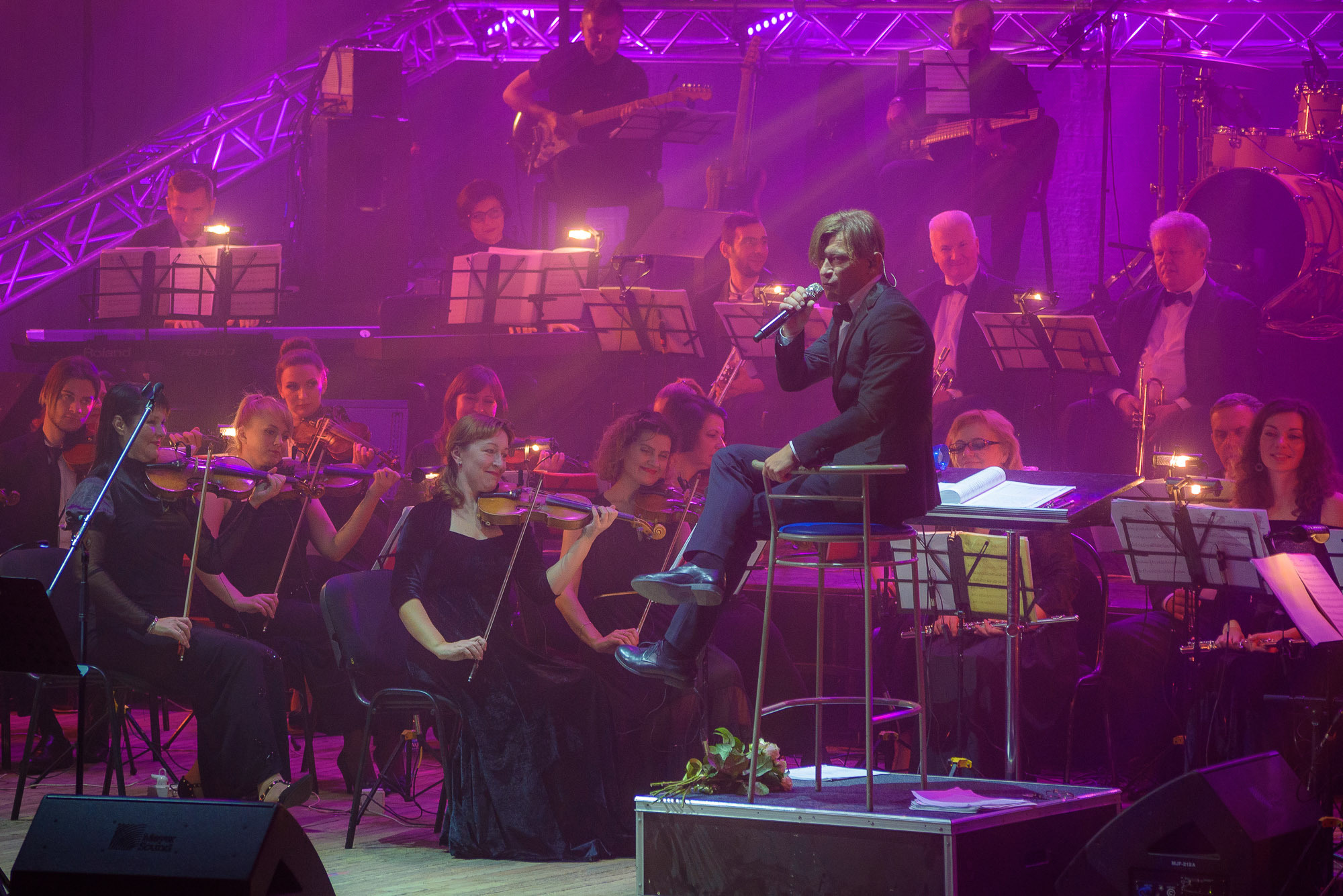 Лёва Би-2 сидит на стуле перед симфоническим оркестром