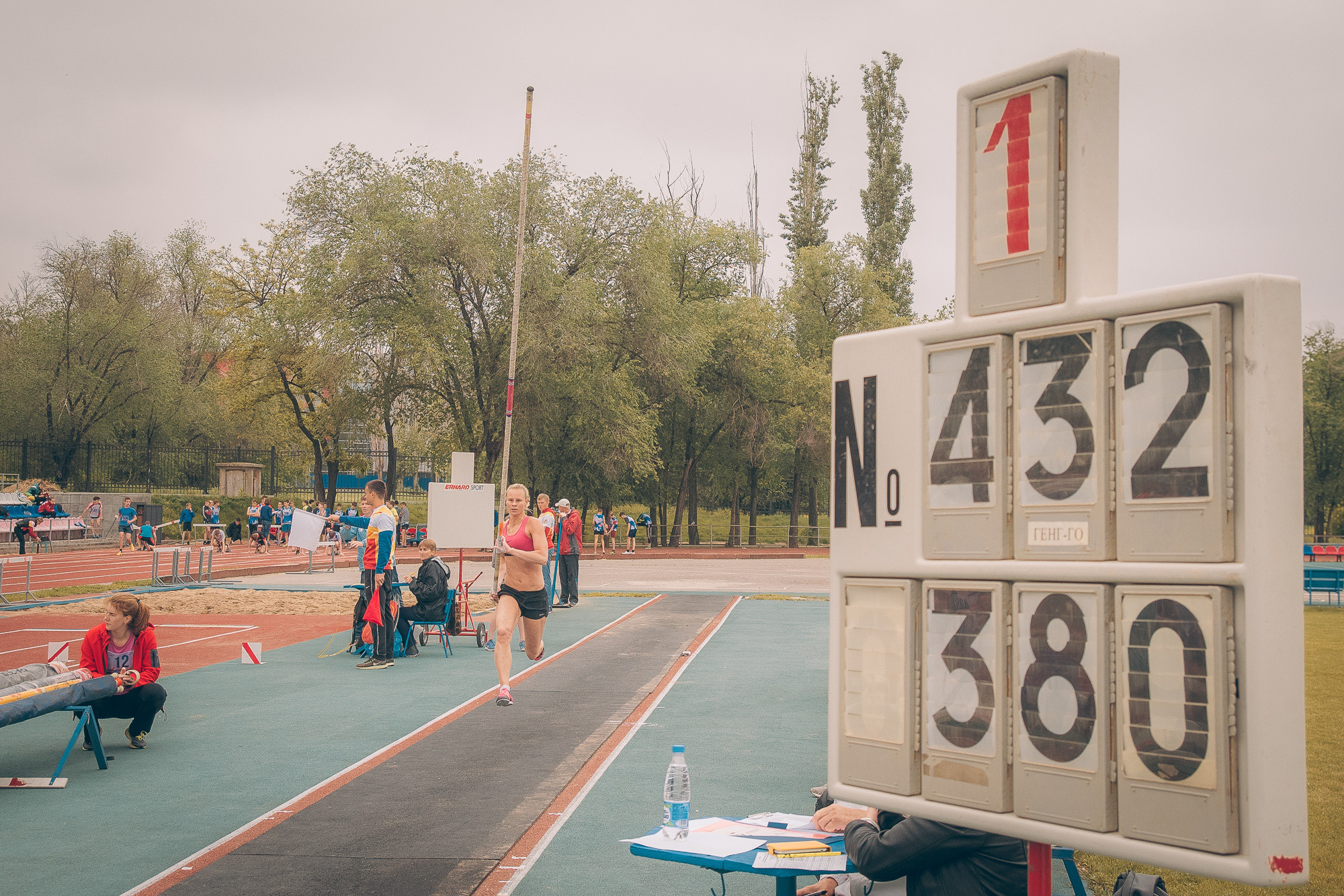Табло легкоатлетических соревнований и бегущая спортсменка с шестом