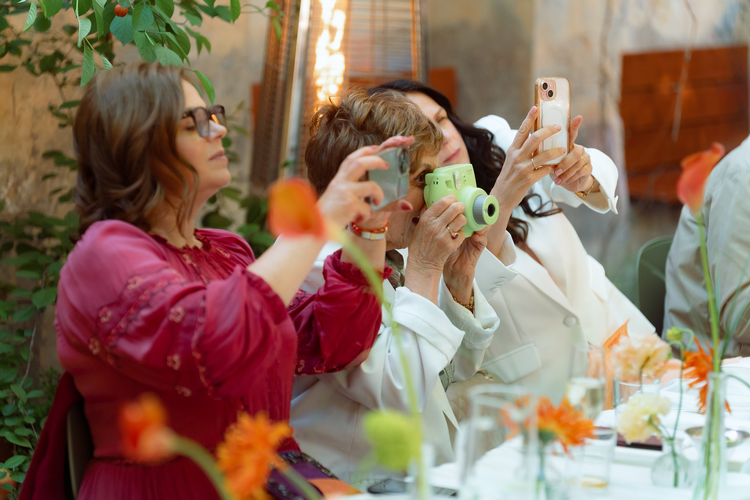 Гостья в красном жакете фотографирует подруг за столом
