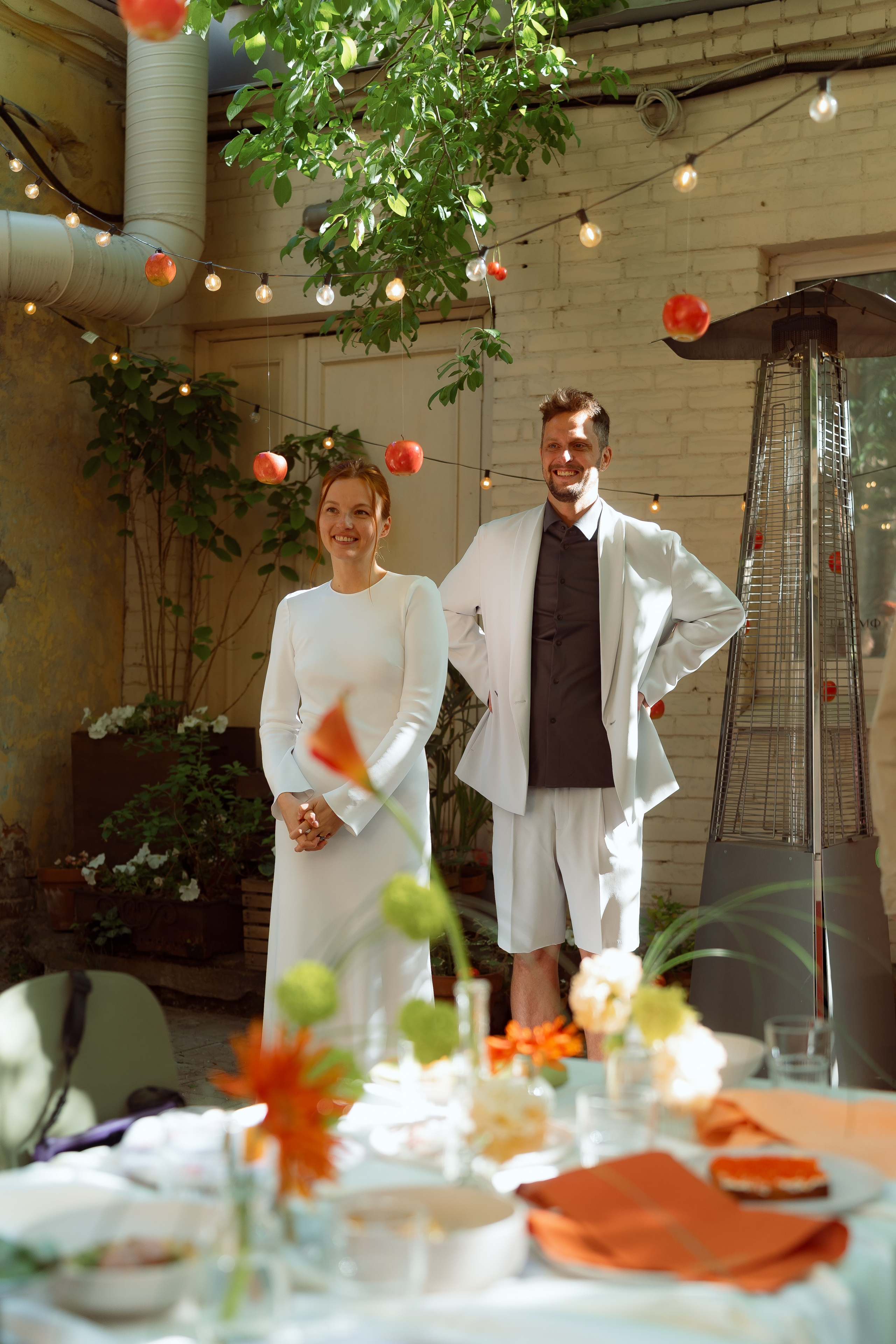 Мария и Евгений выходят во двор под гирляндами, на переднем плане сервированный стол