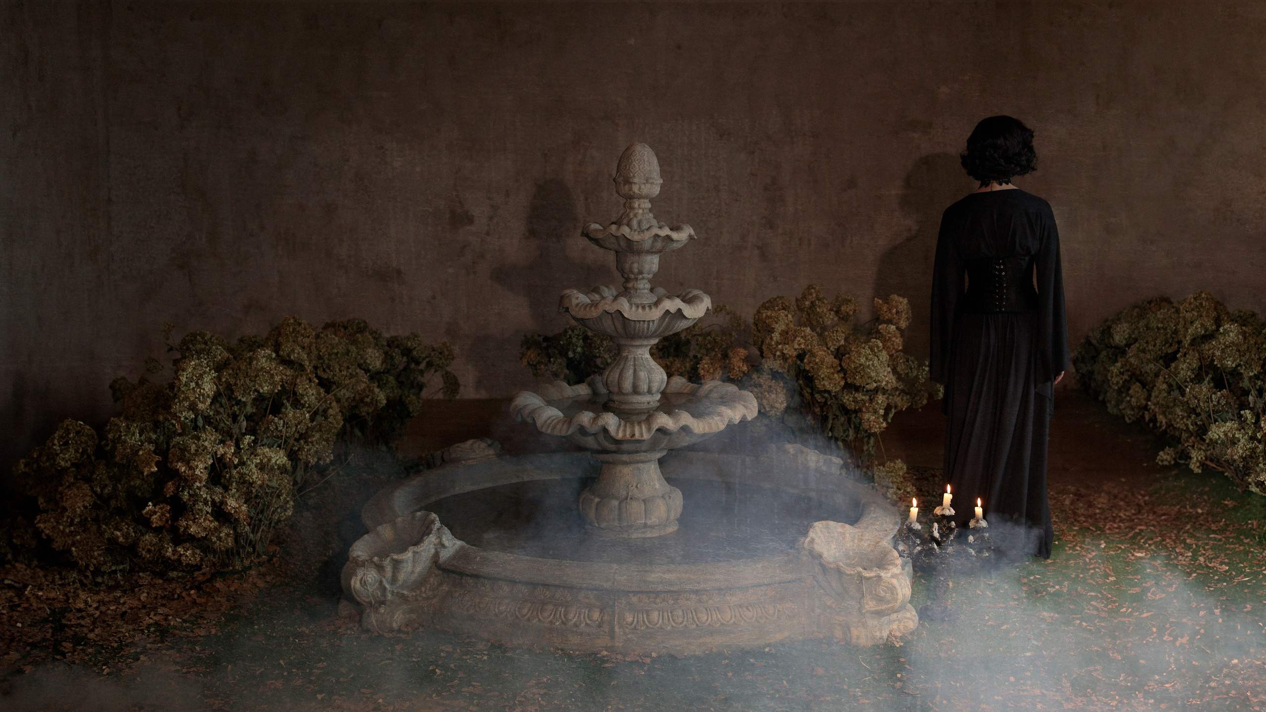 На переднем плане фонтан, девушки уходит вдаль от него, снизу дым, по бокам от фонтана кусты засохших белых гортензий