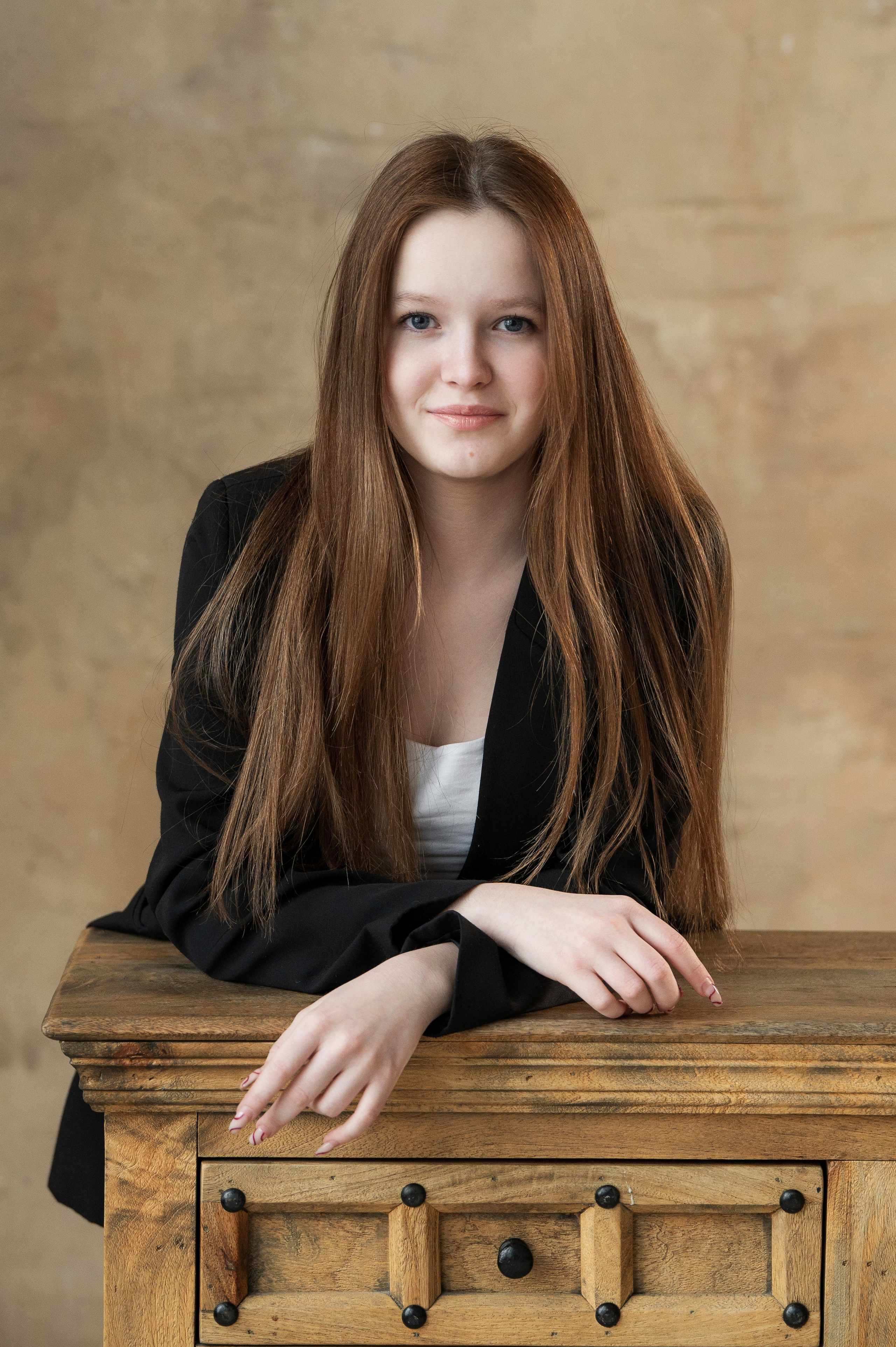 Ученица с длинными волосами позирует у деревянного комода.