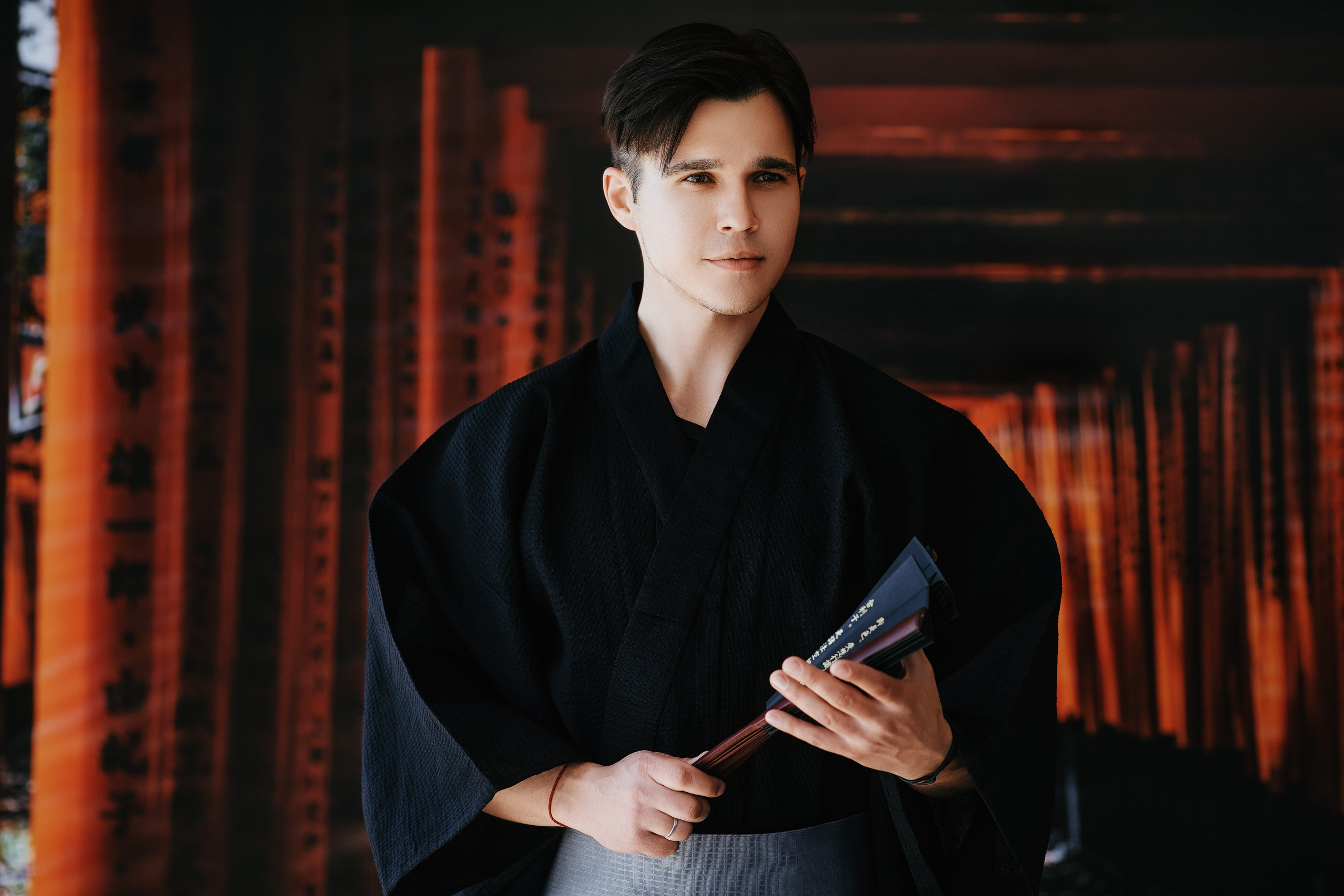 Крутой мужчина в чёрном кимоно с веером в руках позирует на декоративном фоне в японском стиле. Пример стильной фотосессии в Находке