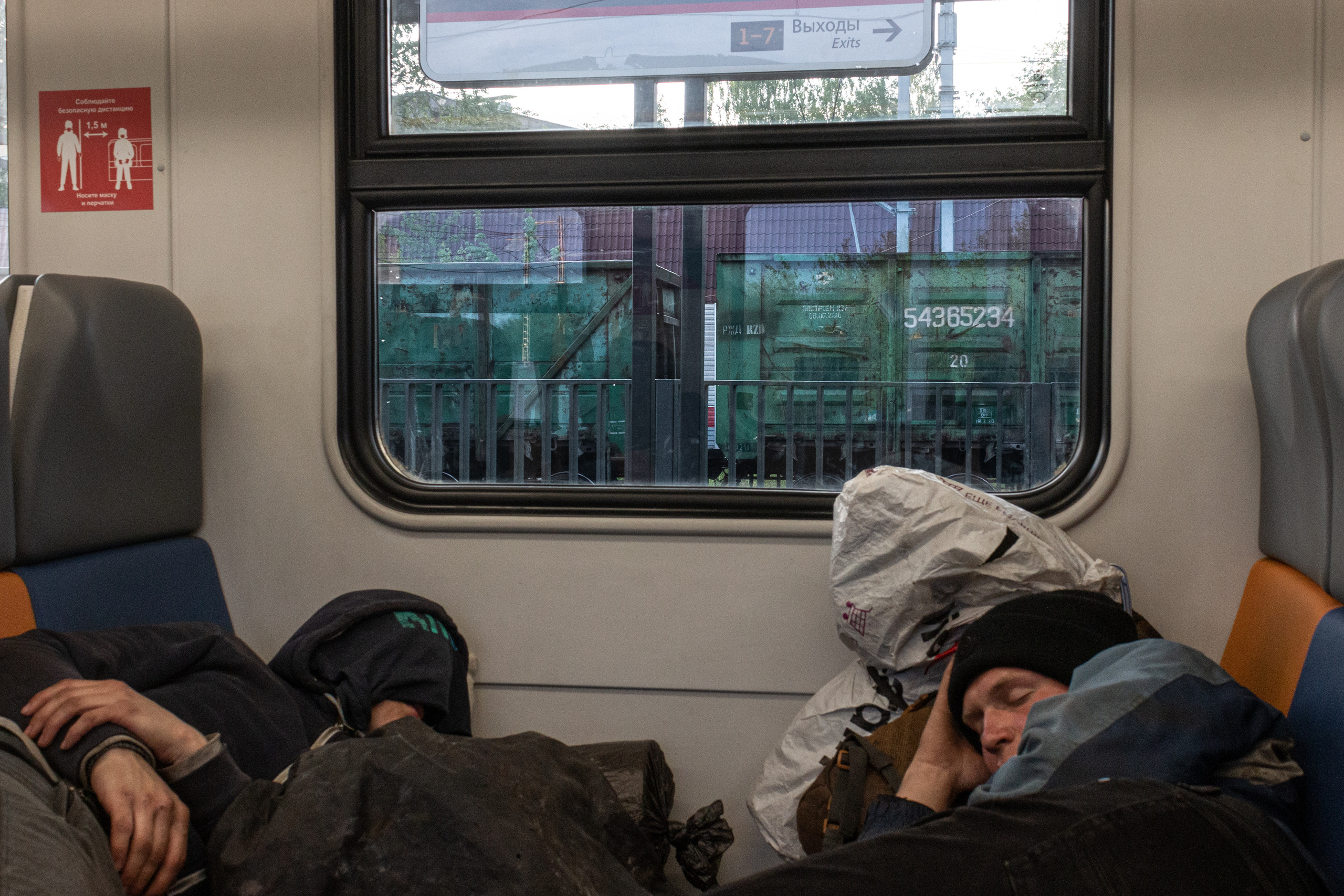 Vlad and Vanya sleeping in the suburban train heading to Moscow. There is a freight train of an unknown marshalling yard outside the window.