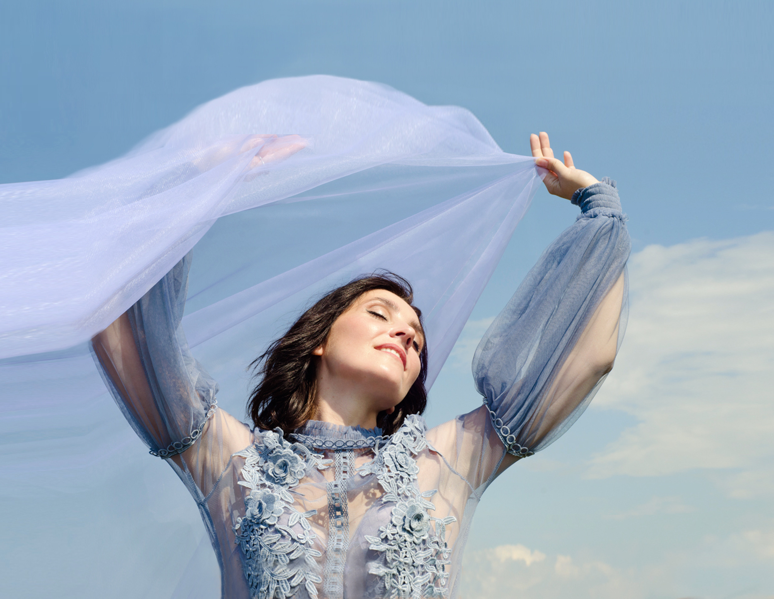 Девушка брюнетка с голубым фатином в мечтах, на фоне неба.