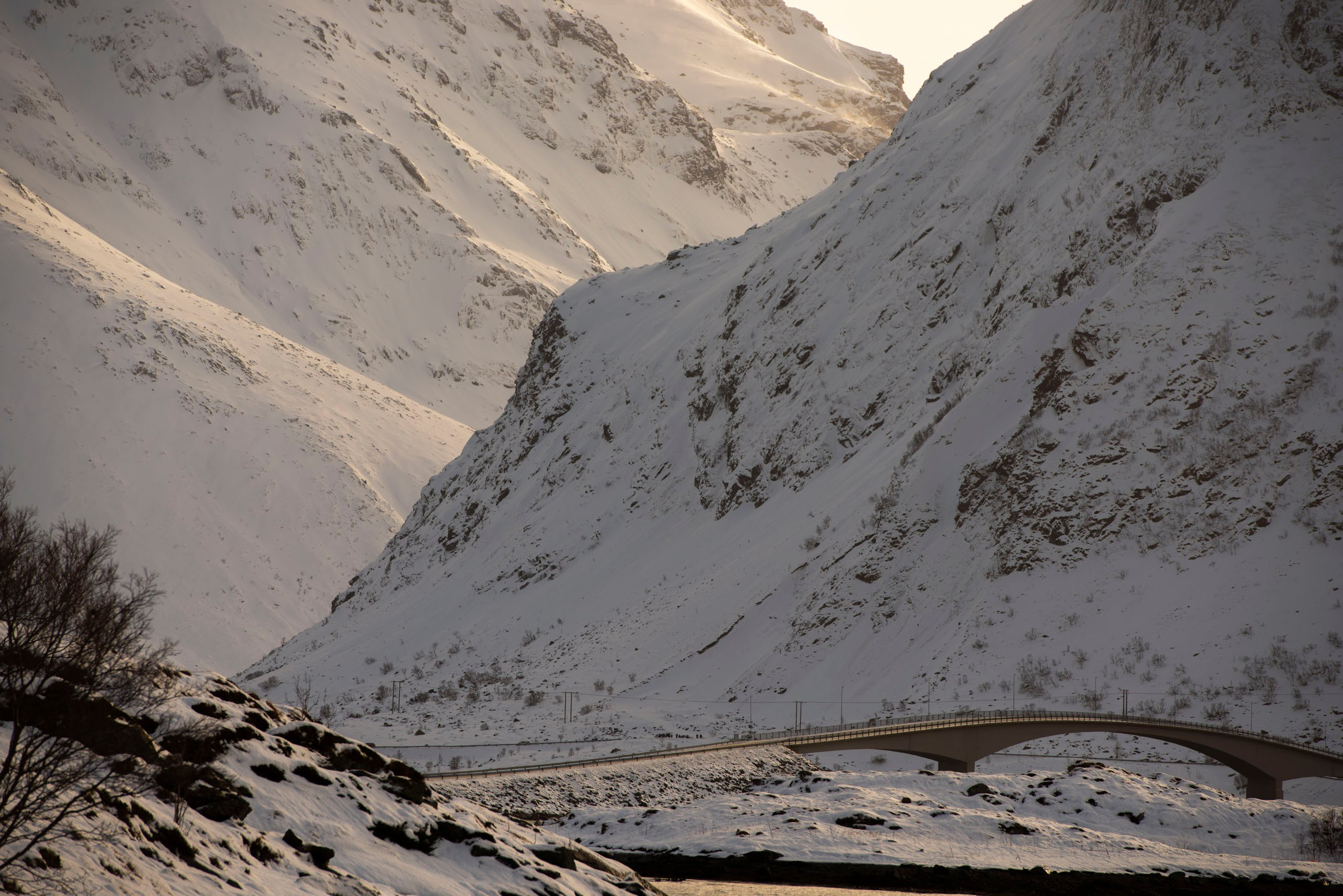 Изогнутый мост Фредванга (Fredvang Bridges) пересекает небольшой водоем, окруженный заснеженными горами на Лофотенских островах, Норвегия.