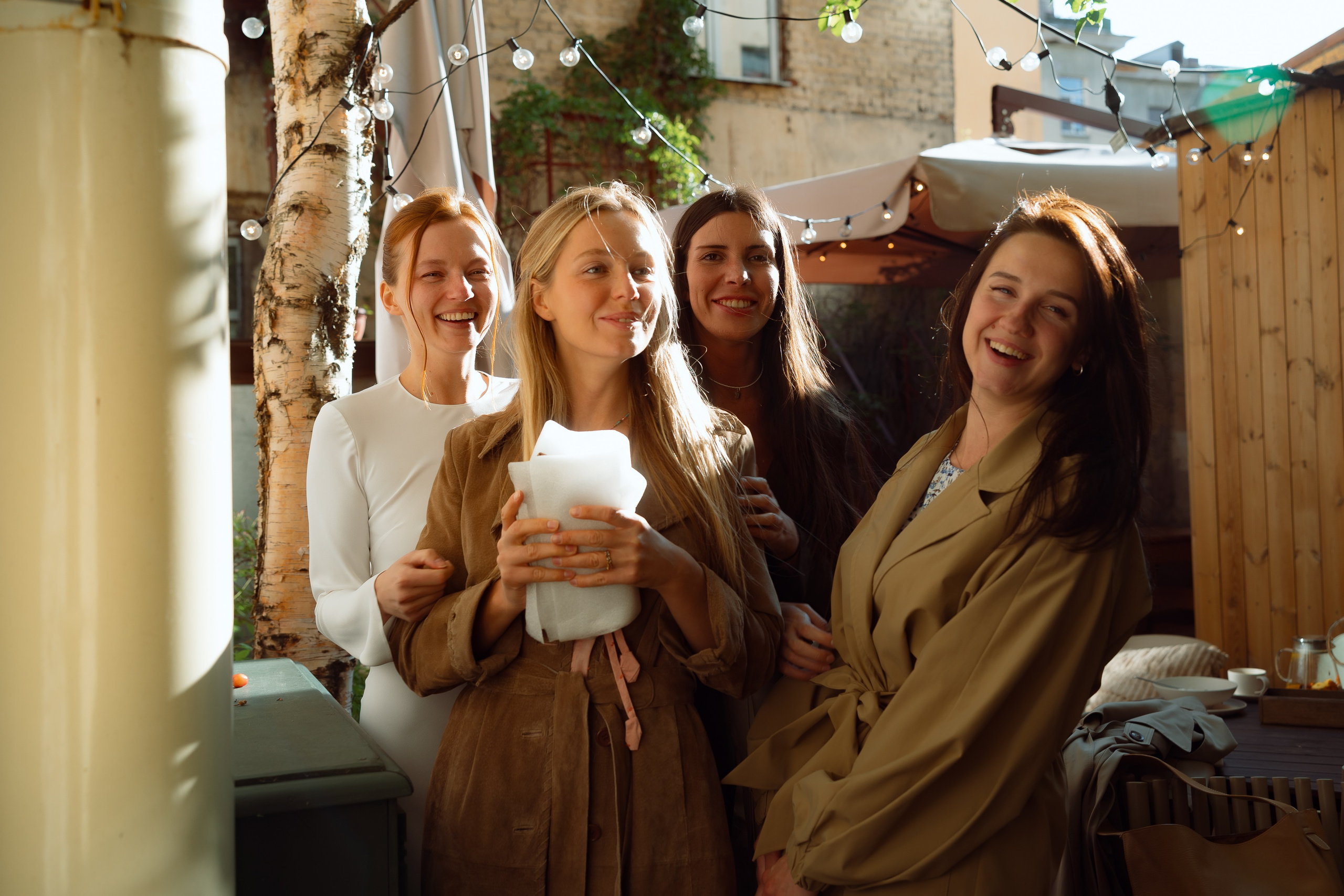 Четыре подруги с чашками кофе улыбаются в саду перед свадьбой