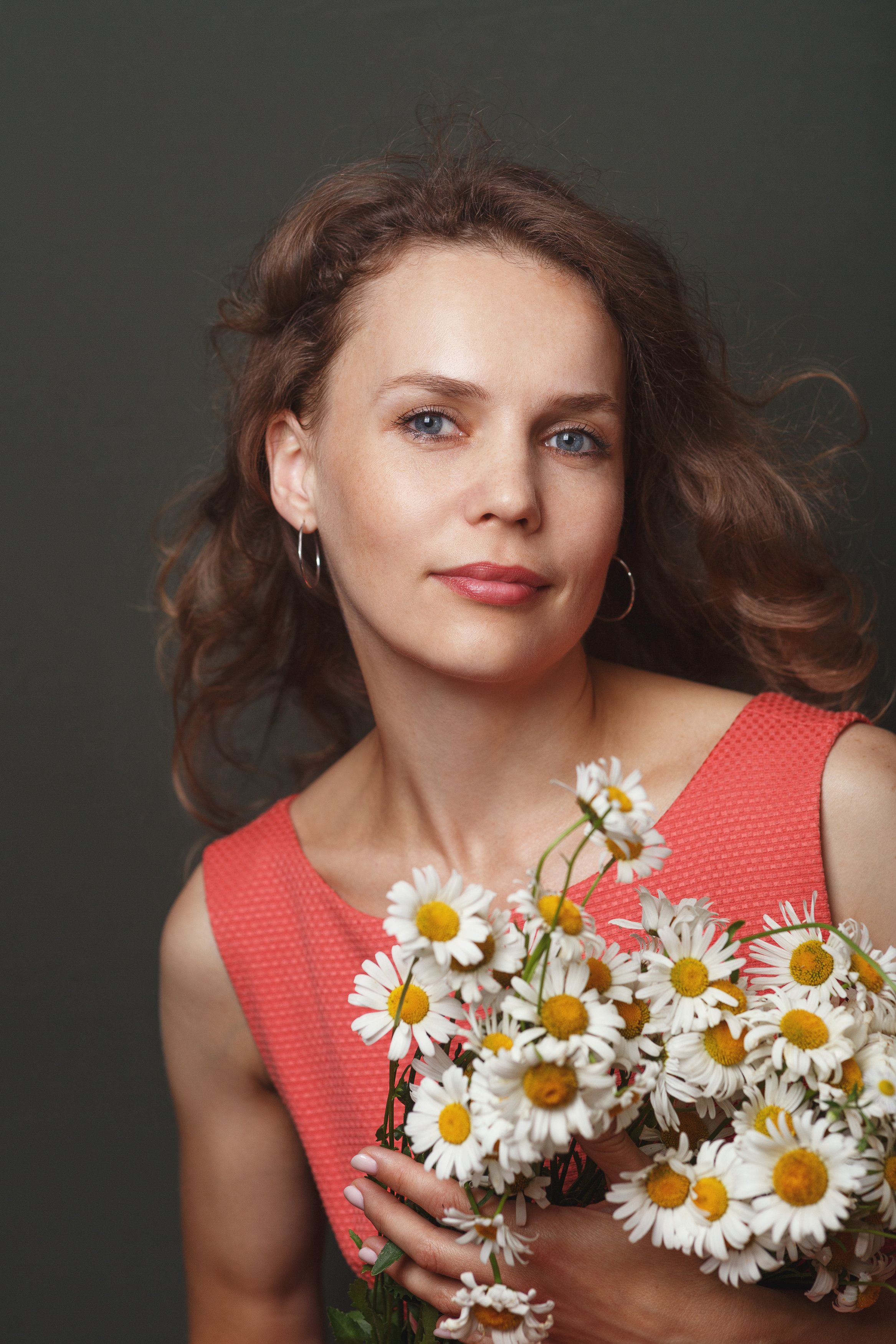 Красивая ,кудрявая, яркая девушка держит букет ромашек в студии.