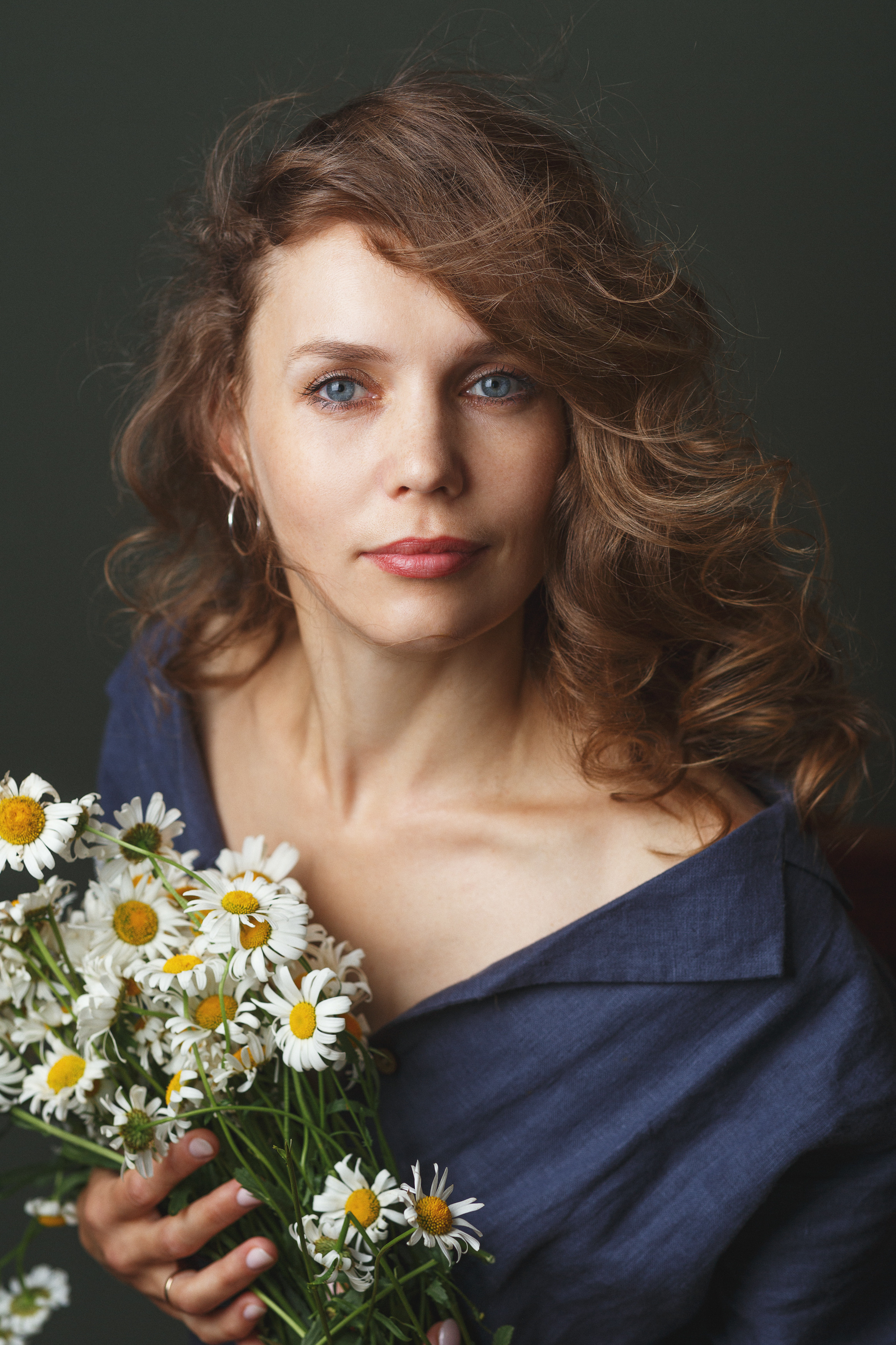 Девушка с длинными вьющимися волосами и синими глазами держит ромашки.
