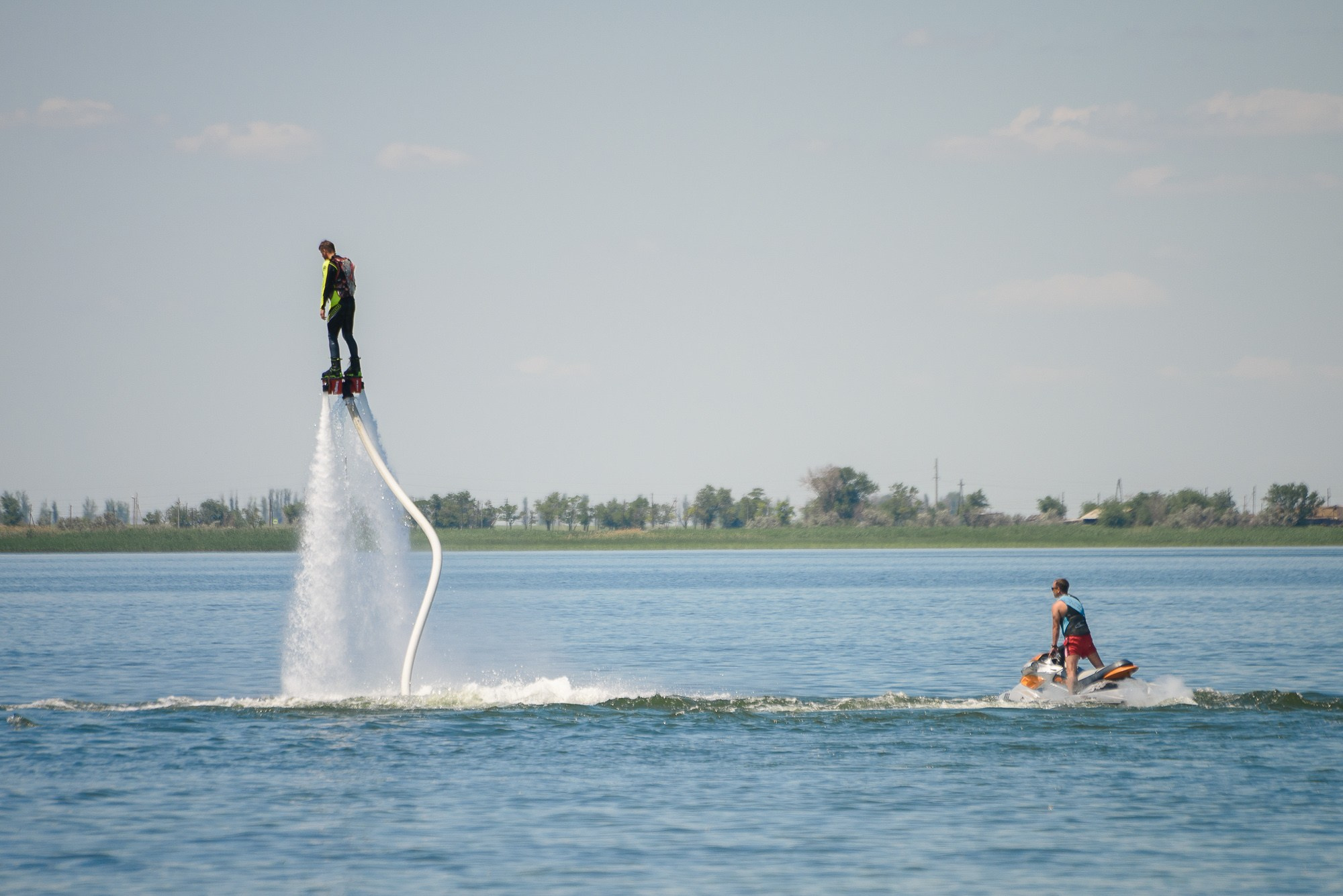 Мужчина на флайборде поднялся над водой и смотрит на человека на гидроцикле