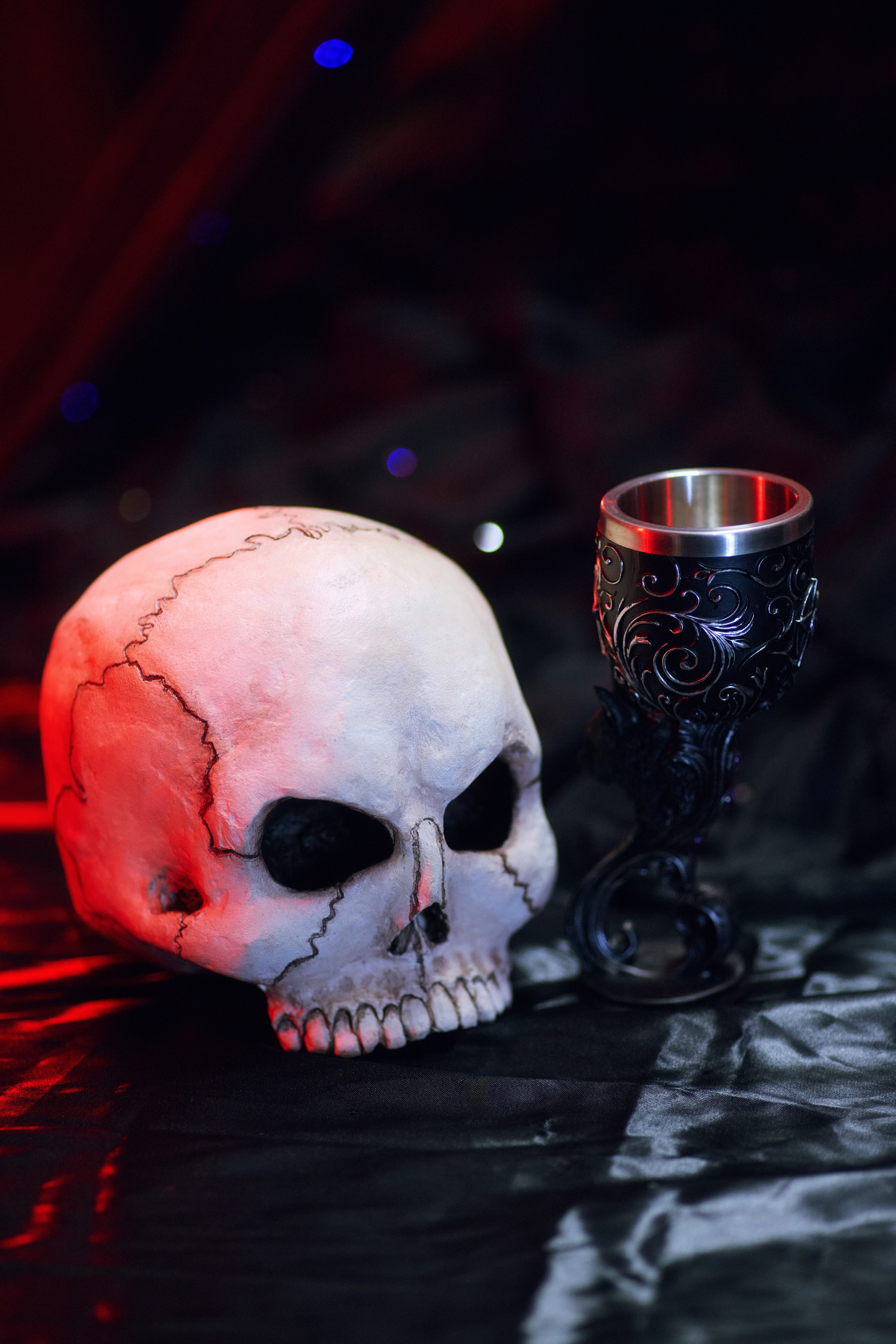 Череп и бокал на фоне чёрной ткани с красной подсветкой