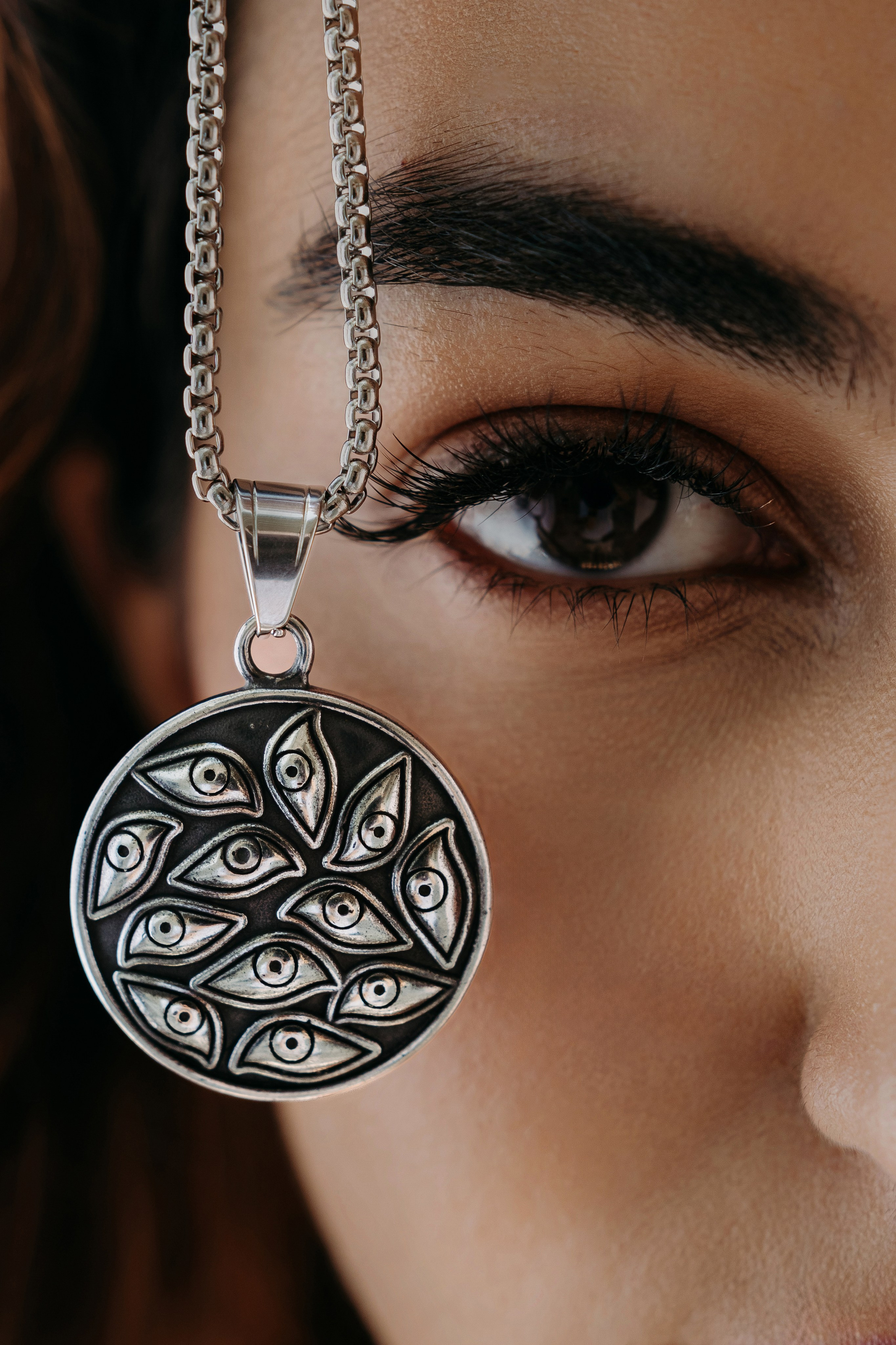 Detailed shot of a silver pendant necklace with a unique pattern, styled elegantly near a model's eye.