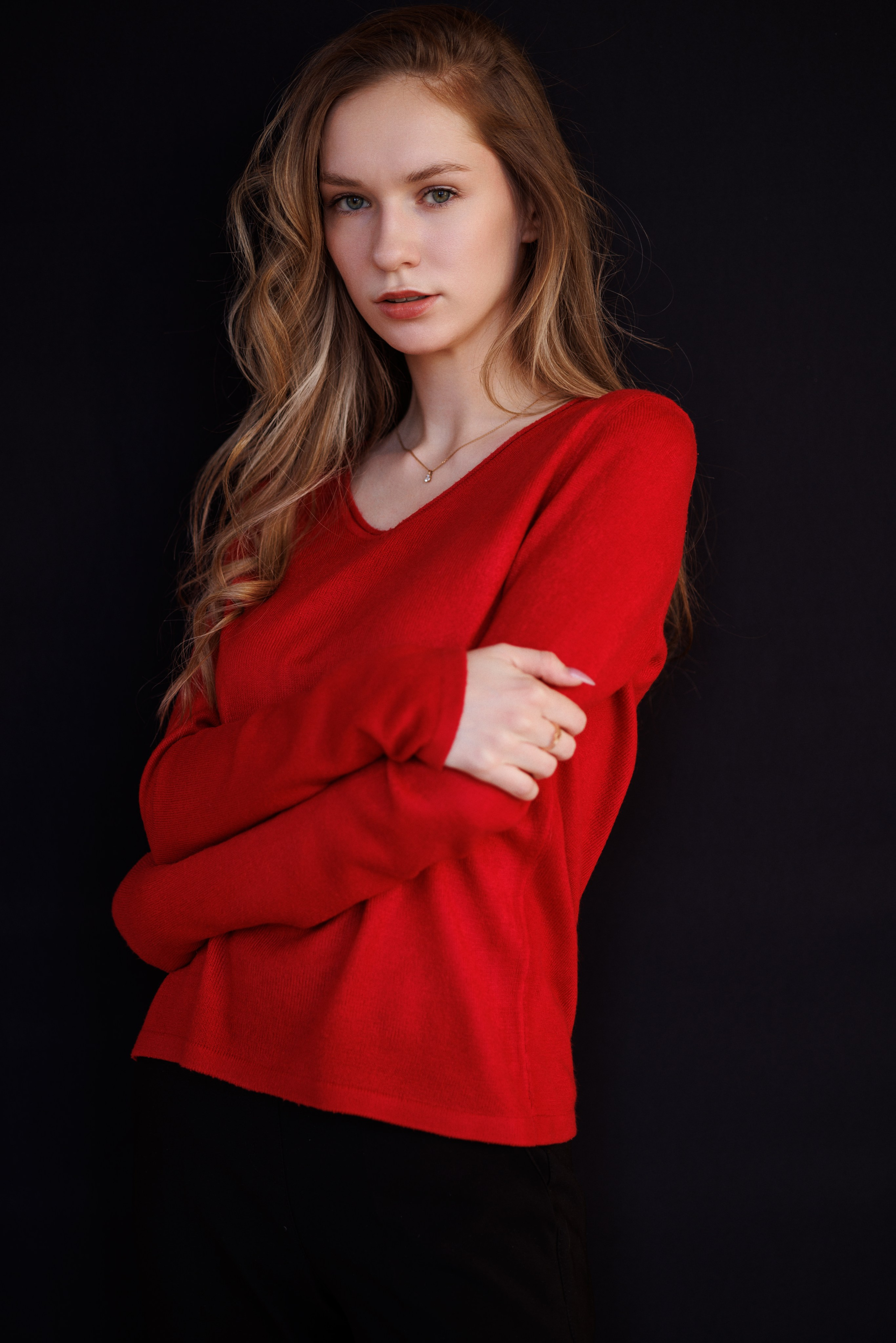 Женский поясной портрет девушки к красном свитере с длинными светлыми волосами на черном фоне. Снято в студии с импульсным светом
