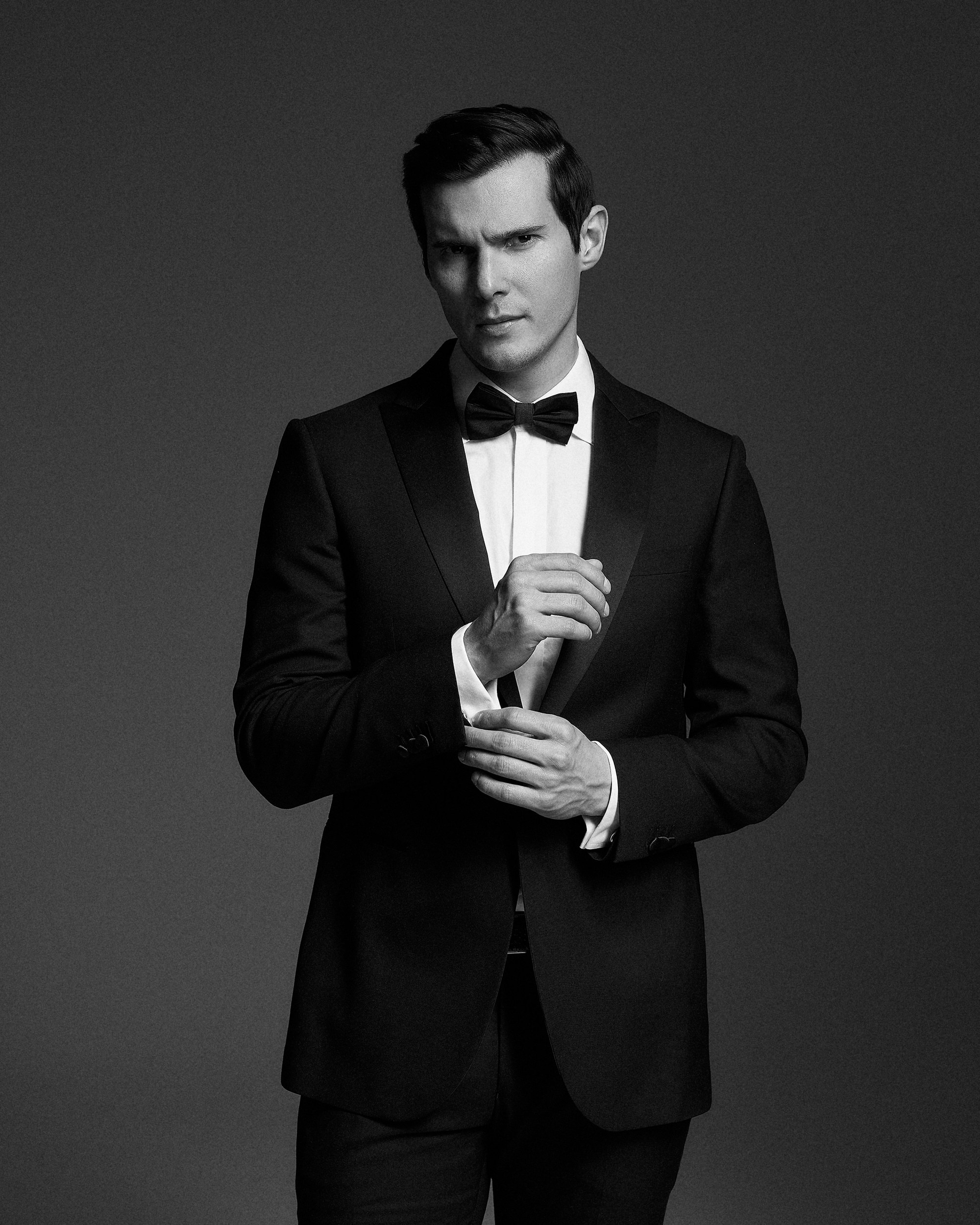 Портрет жениха в смокинге на тёмном фоне студии. Сдержанный взгляд, чёткие линии костюма, чистый свет. Свадебная съемка в минималистичном стиле, фотограф Дмитрий Цветков, Санкт-Петербург