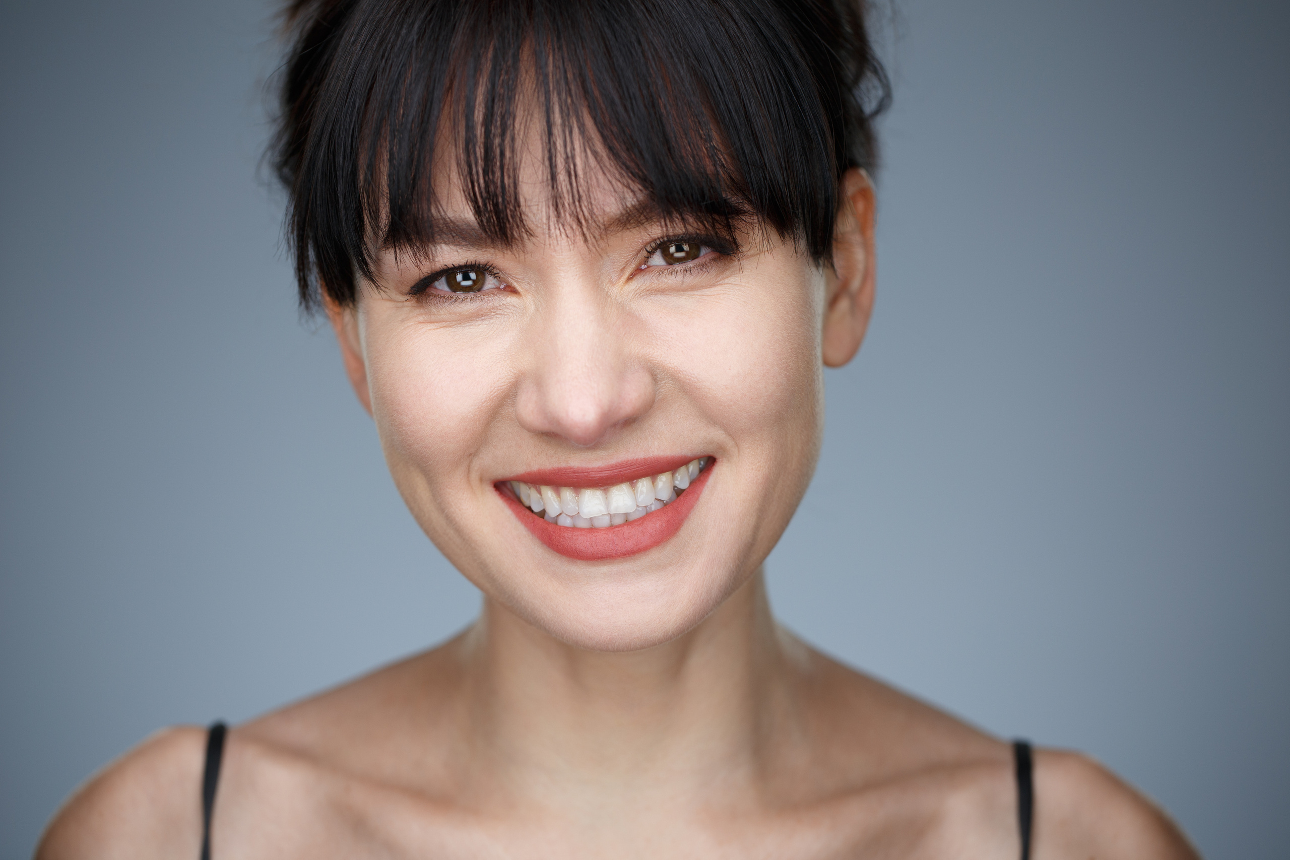 Хедшот. Деловой портрет молодой улыбающейся женщины на сером фоне.