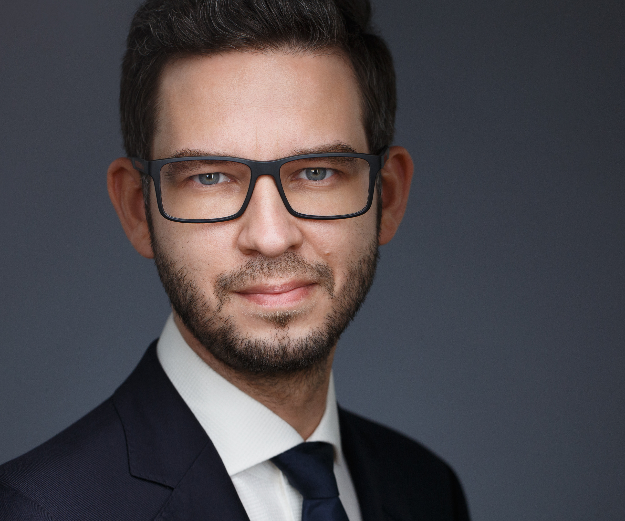 Бизнес-портрет мужчины в очках на тёмном фоне.