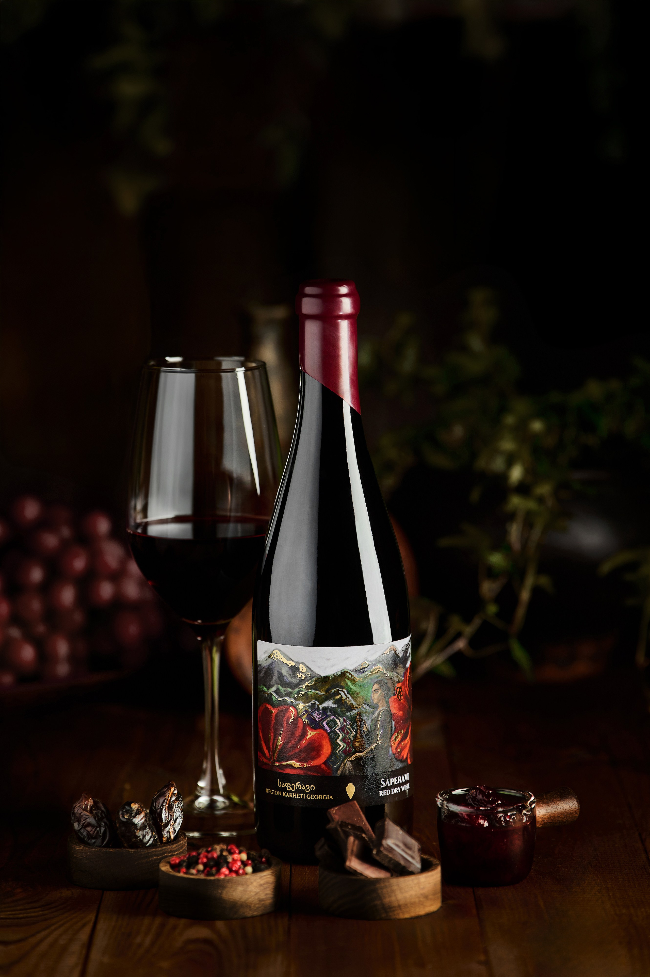 Бутылка красного вина с декоративной этикеткой и бокалом на фоне темных виноградных гроздей