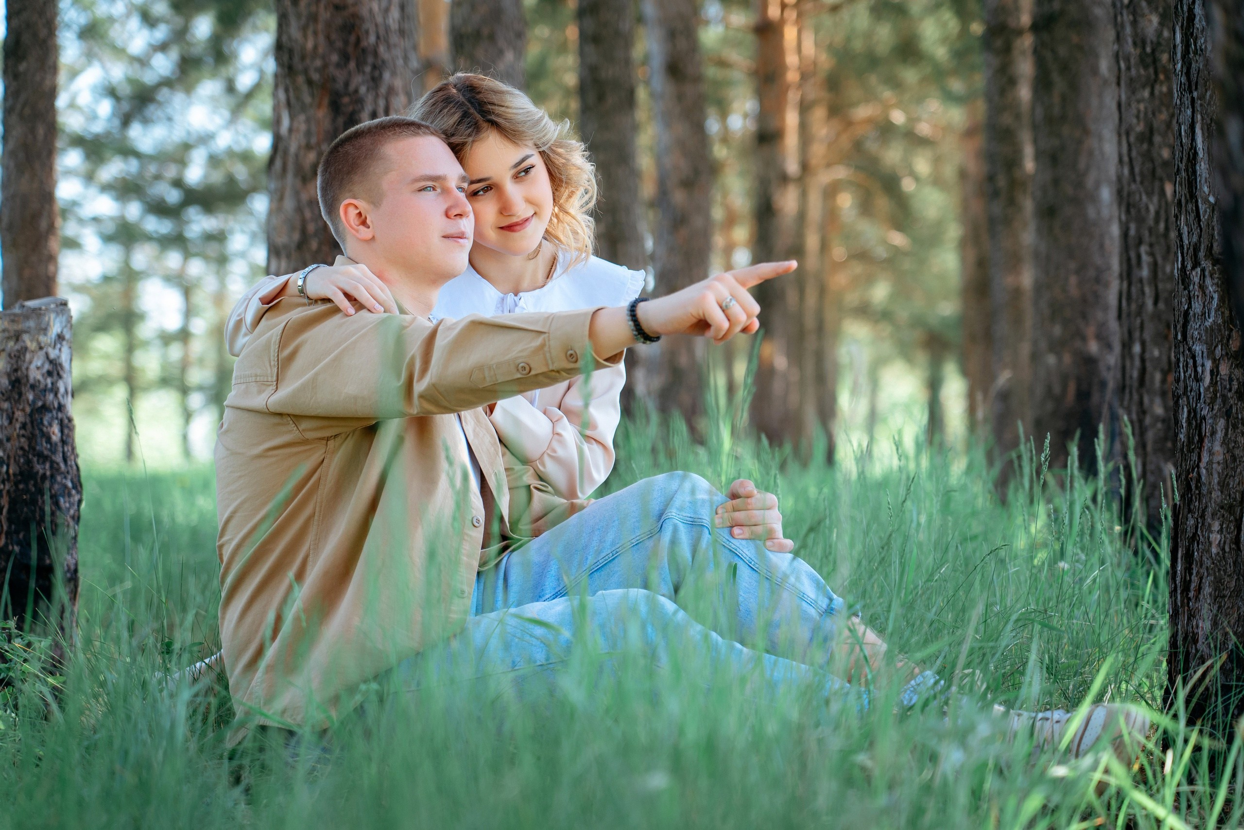 Love story в сосновом бору, парень показывает девушке на закат солнца