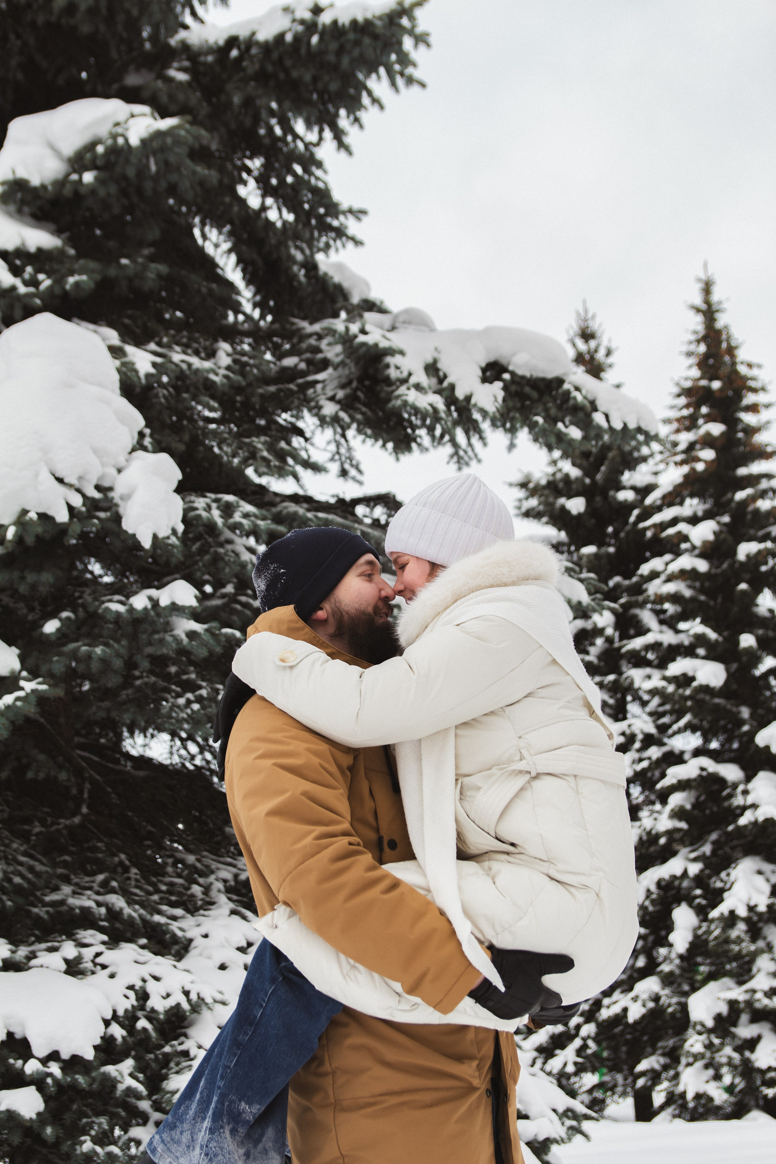 Фотосессия на природе - пара обнимается зимой в заснеженном хвойном лесу