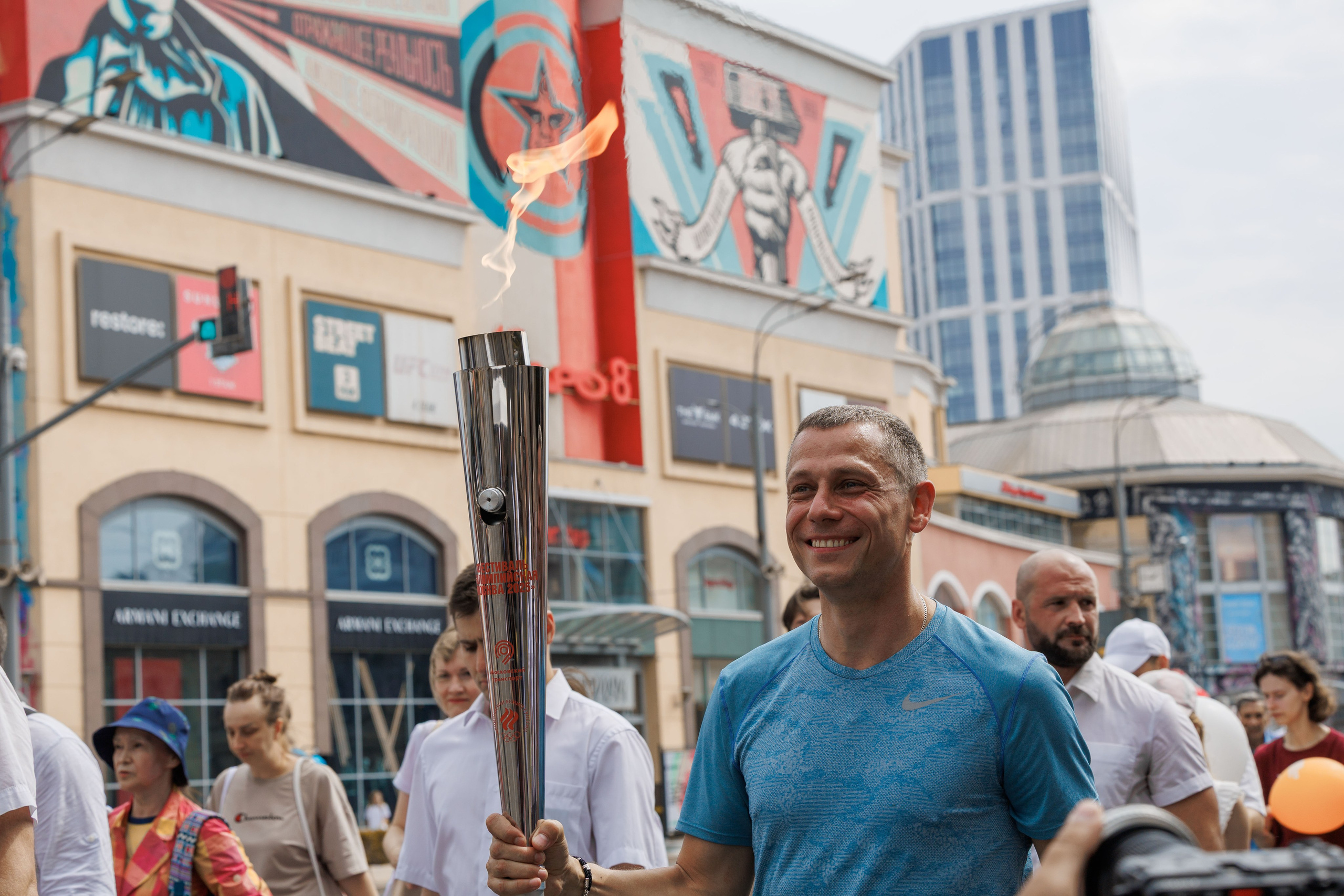 Юрий Борзаковский несет Олимпийский огонь по Садовому кольцу на фоне фото СССР