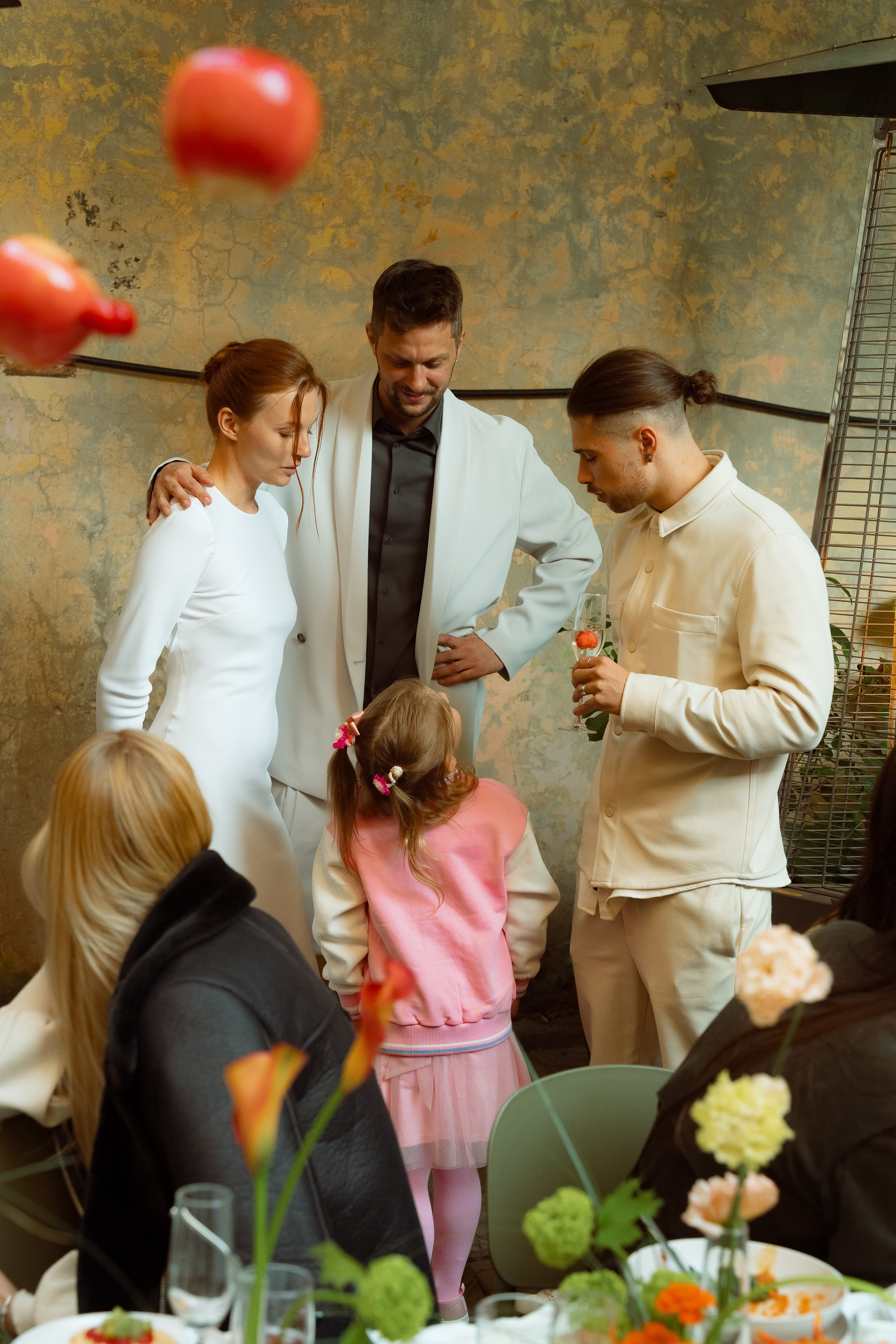 Группа гостей слушает речь ведущего под гирляндами во дворе