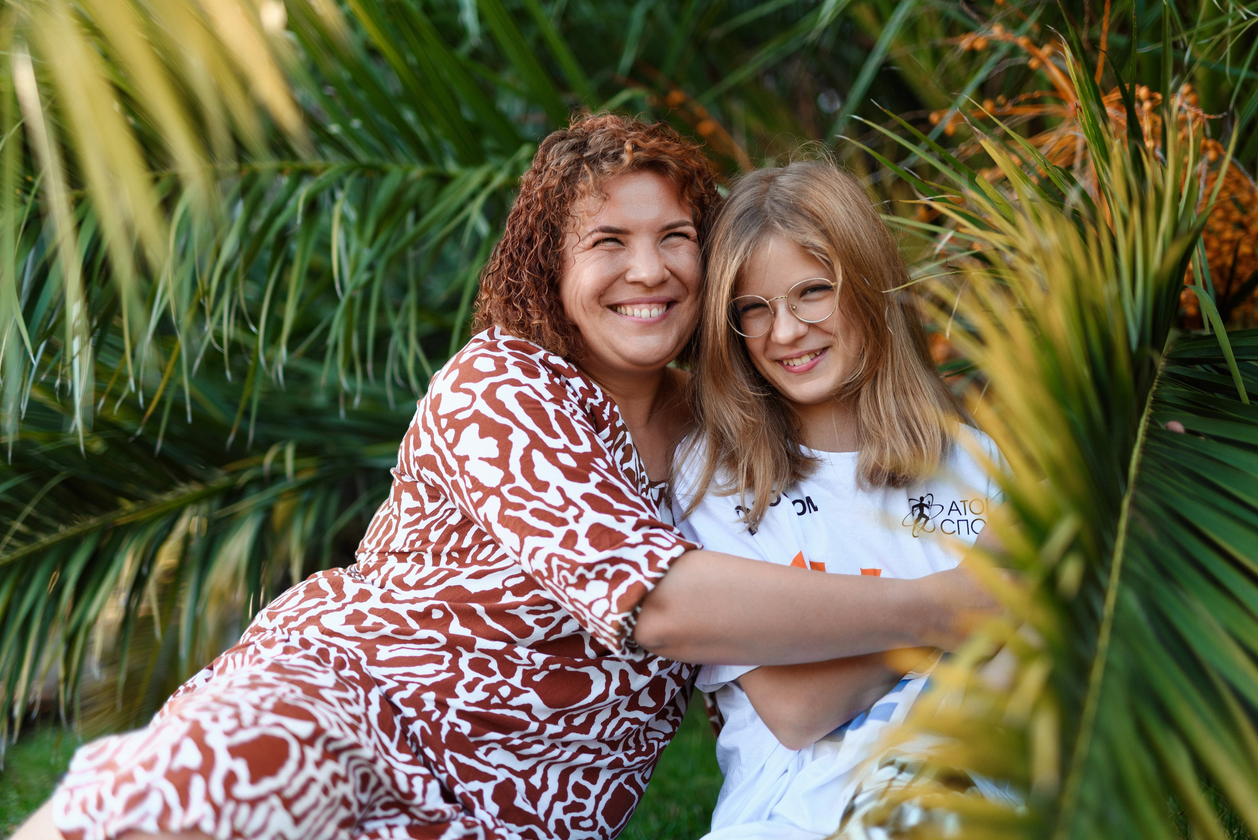 Мама и дочка обнимаются на фоне пальмы