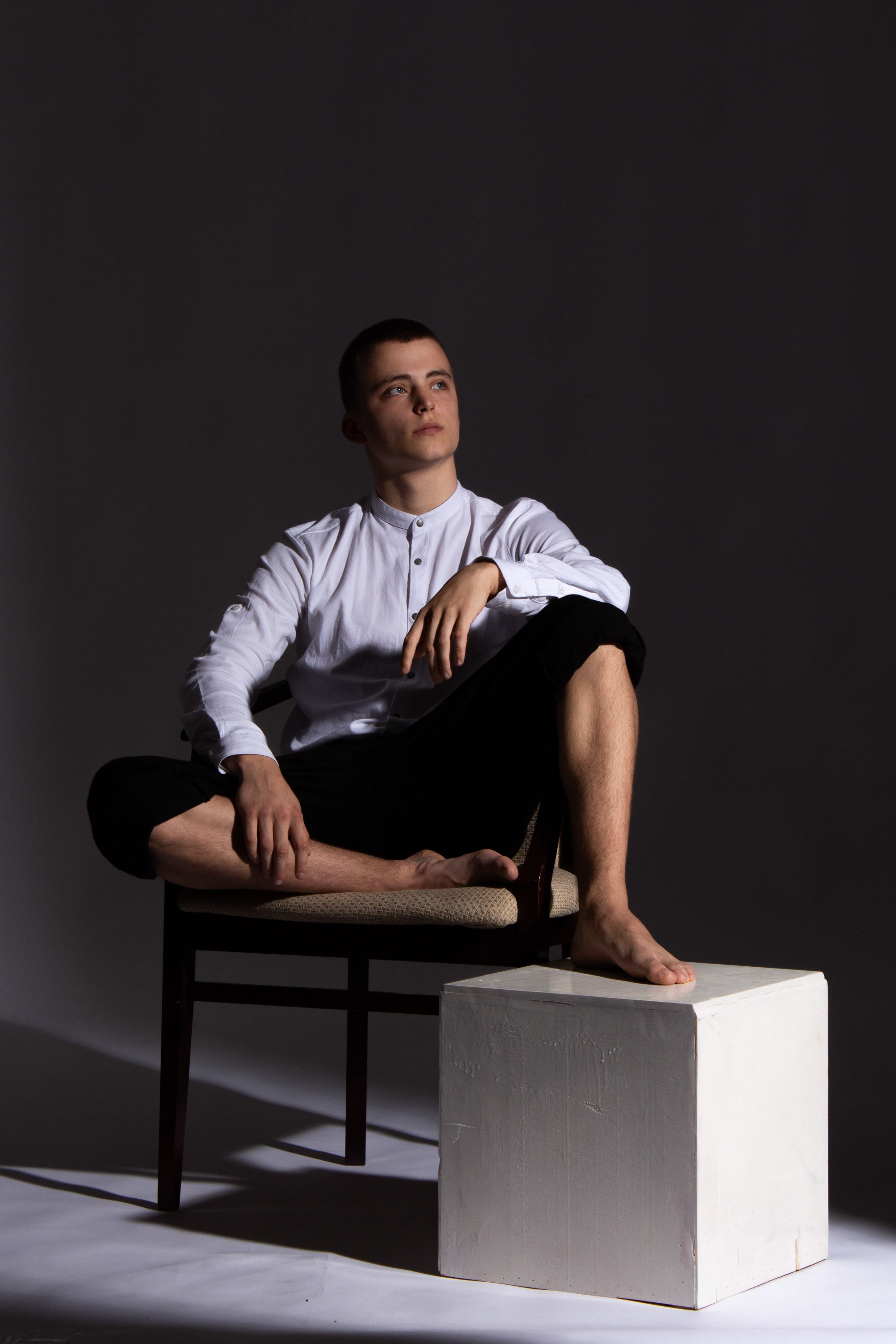 Парень сидит на стуле, поджав ноги. Студийная съёмка Астрахань.