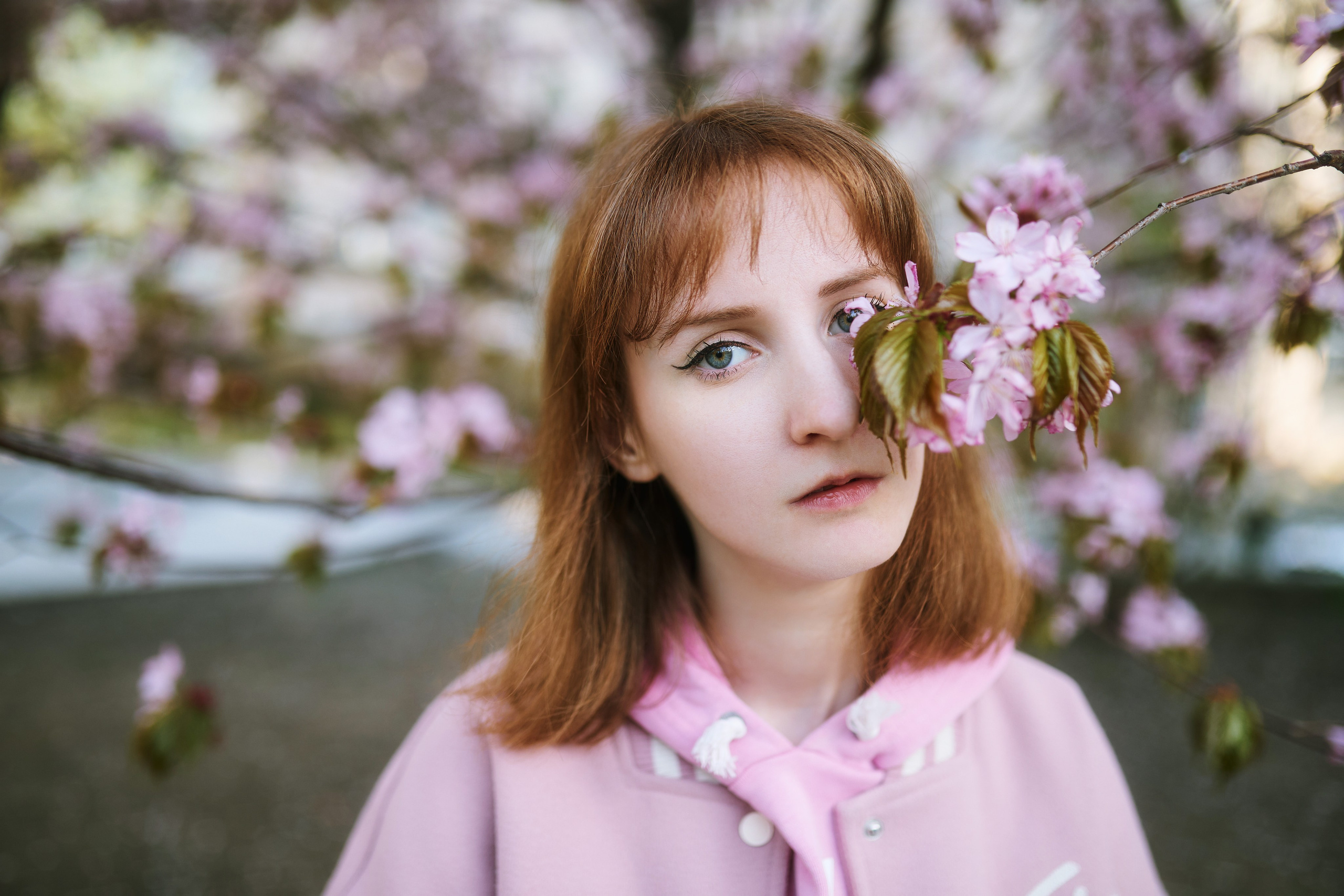 Портретная фотосессия с цветами во Владивостоке неподалёку от театра имени Максима Горького. В центре кадра - молодая девушка, прикрывающая один глаз розовыми лепестками.