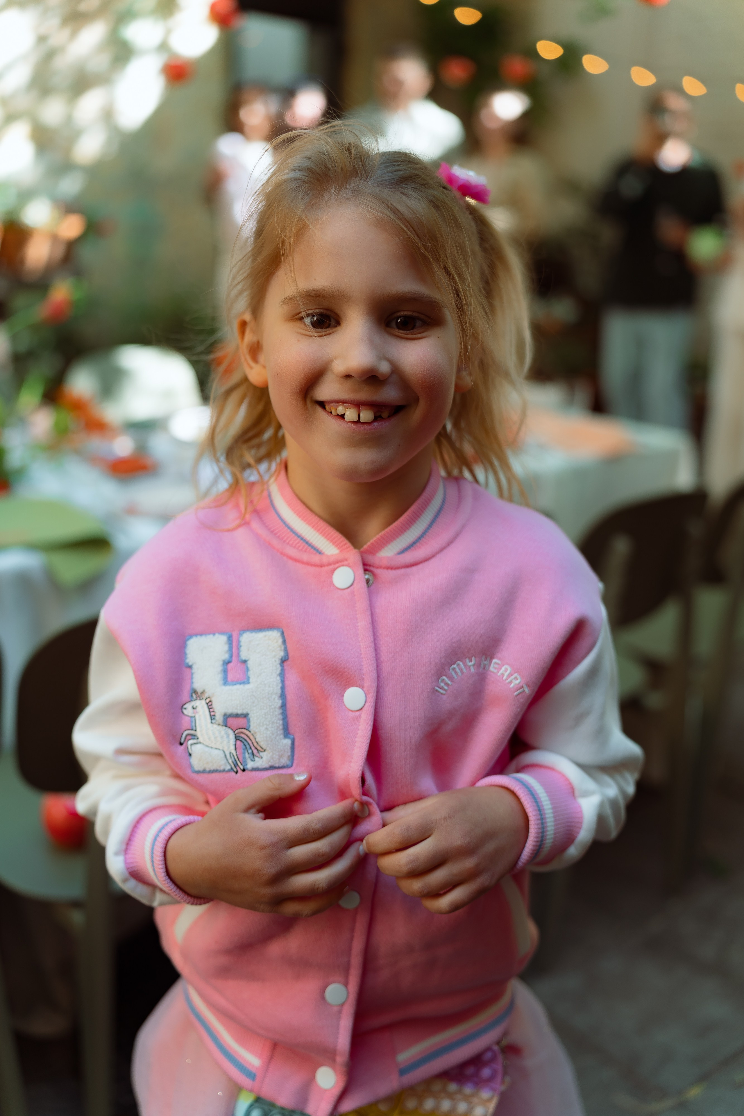 Девочка в розовой олимпийке с буквой H улыбается на банкетной площадке