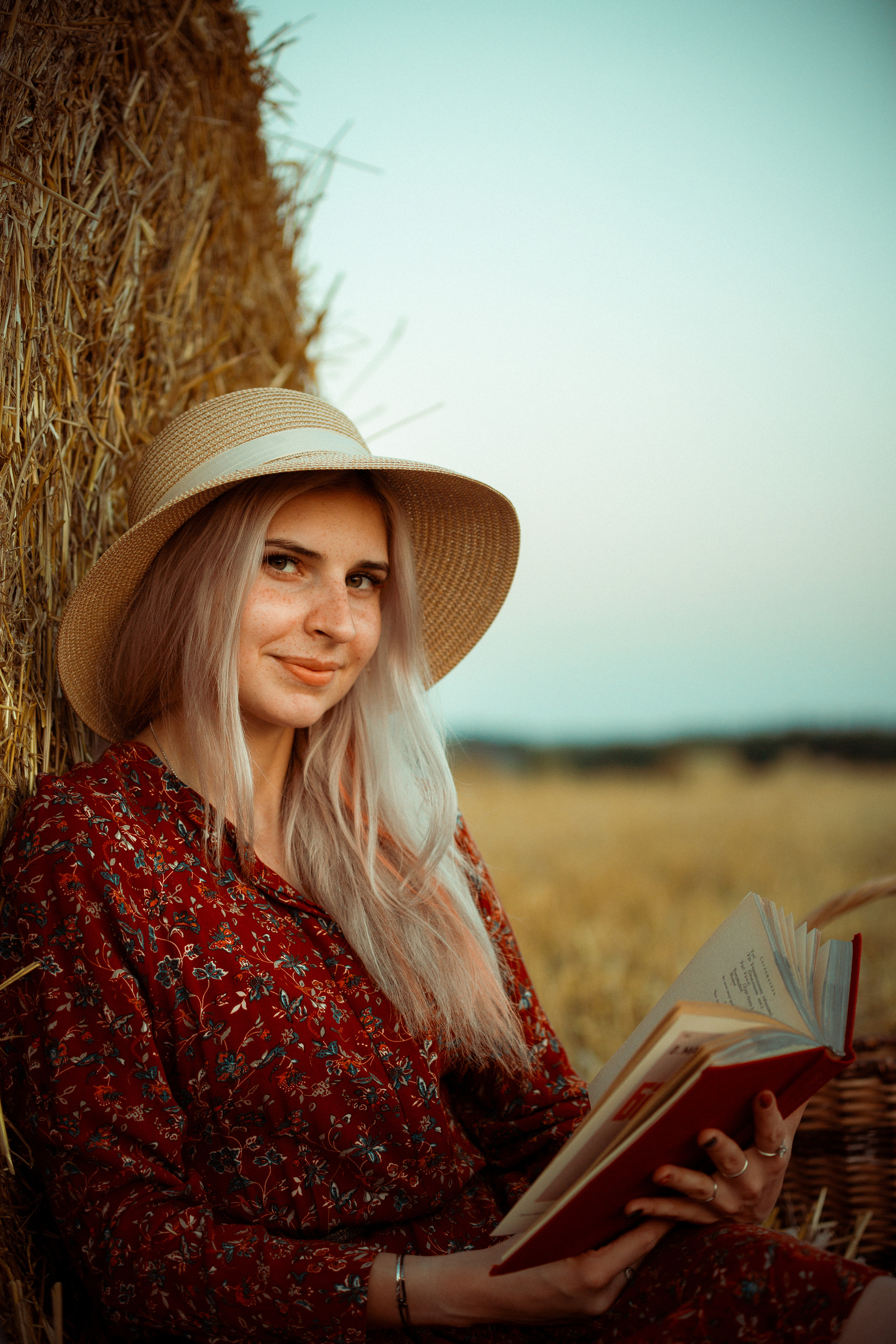 Девушка в поле возле рулона сена с книгой
