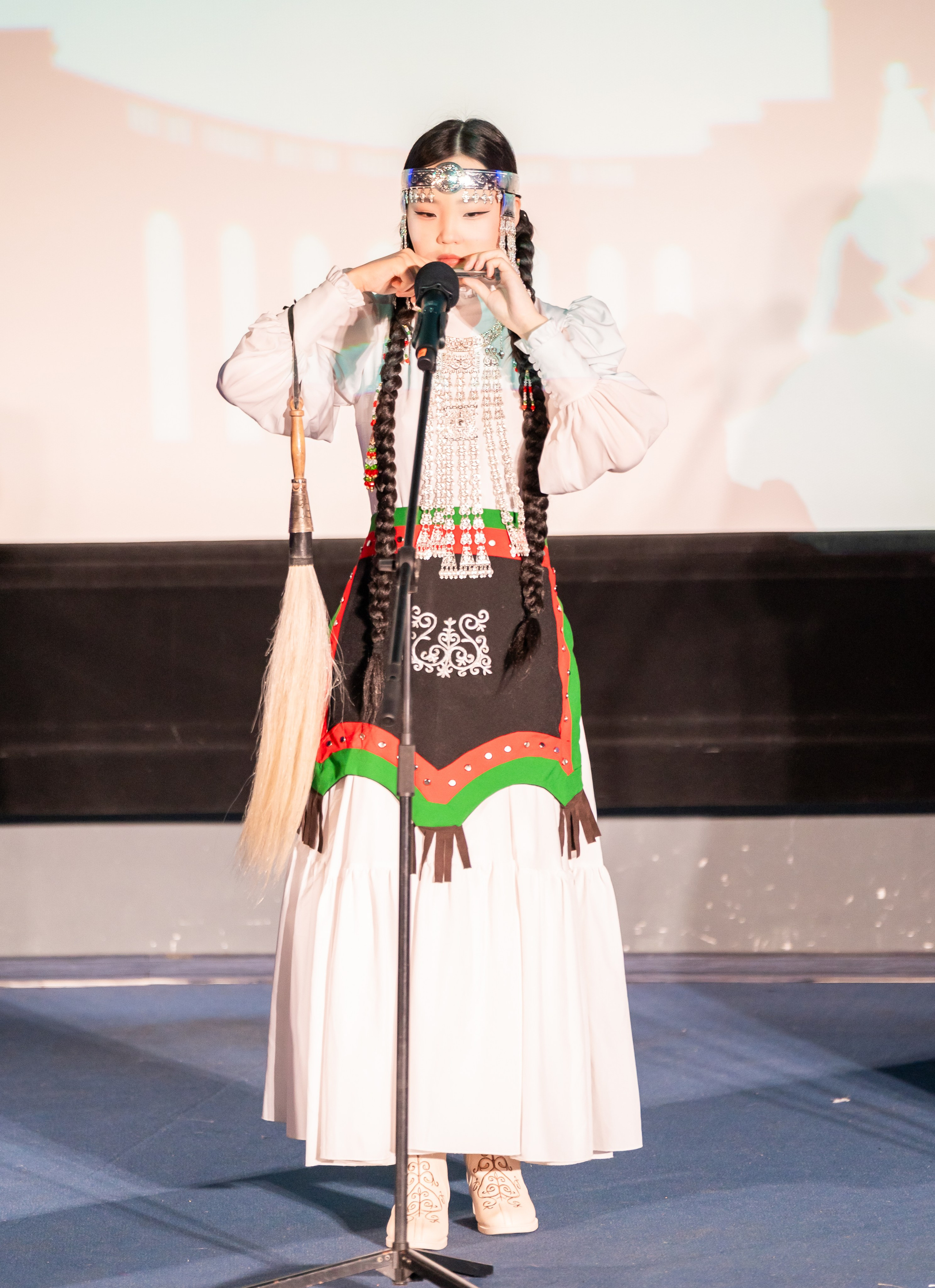 12 Международный фольклорный фестиваль Сохраняем традиции. Девушка в красивом традиционном костюме с орнаментом играет на варгане (хомусе). Фольклорное выступление на сцене. Автор: Евгений Мальцев (evrednix.ru).