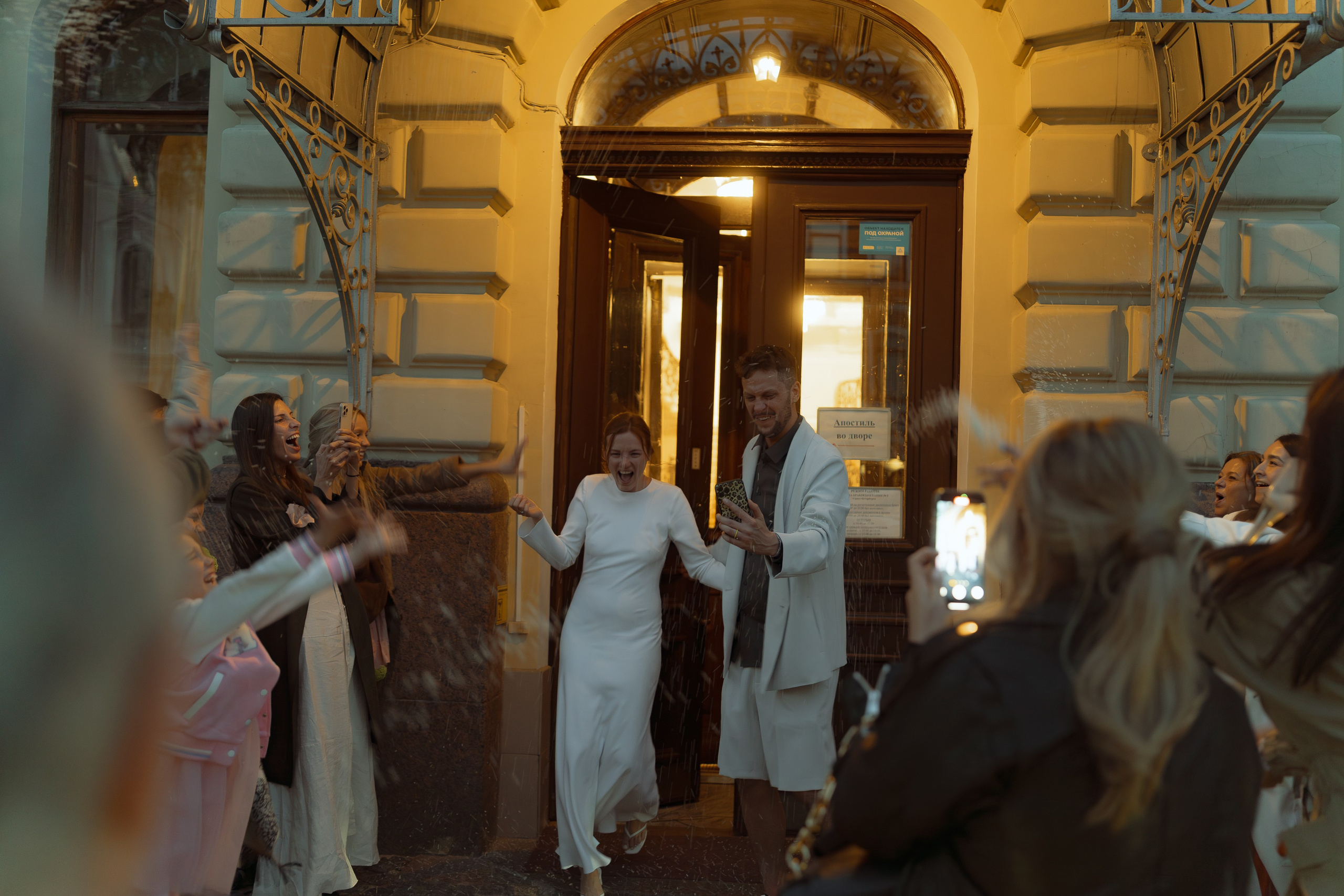 Мария и Евгений выходят из дверей ЗАГСа вечером, гости выстроились коридором аплодисментов