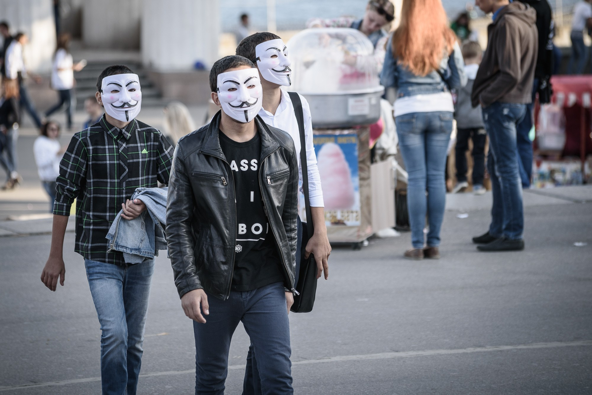 Три молодых человека в масках Анонимусов идут по набережной