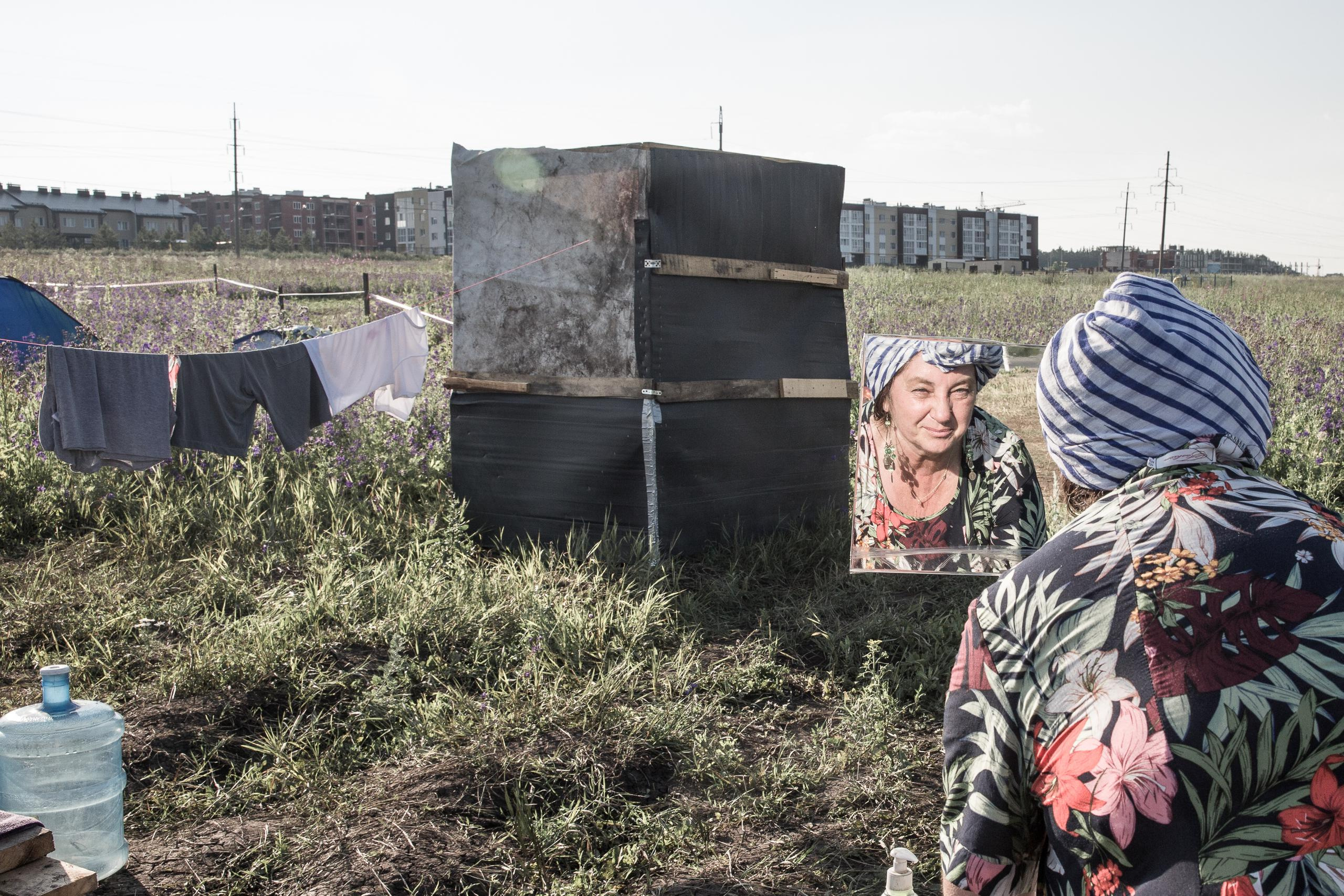 Люба моет руки и смотрится в зеркало в палаточном лагере.