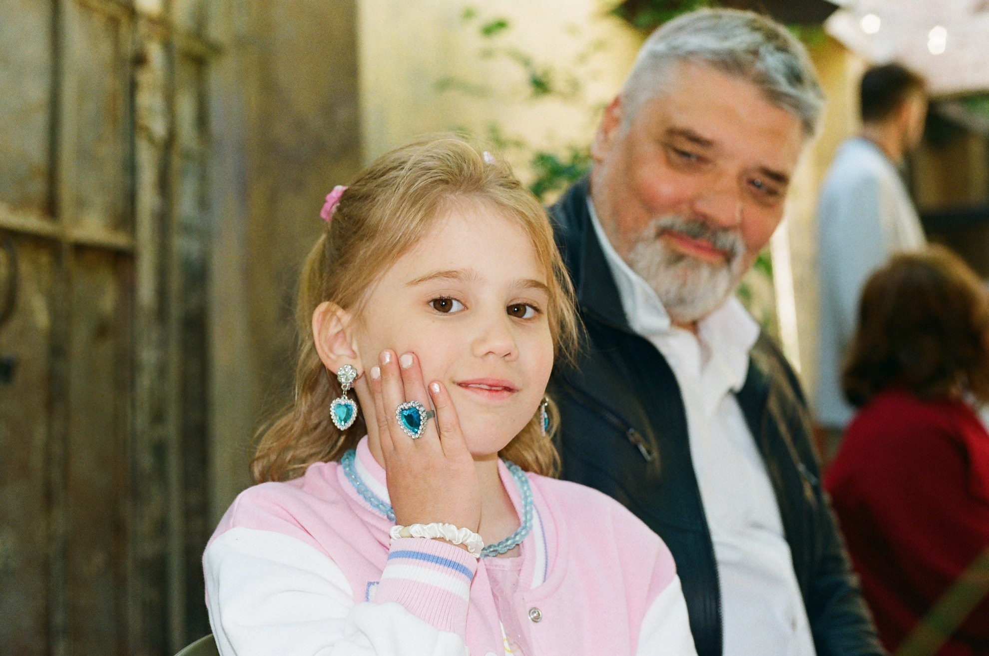 Юная гостья поправляет серьгу, улыбается, плёнка подчеркивает эмоции