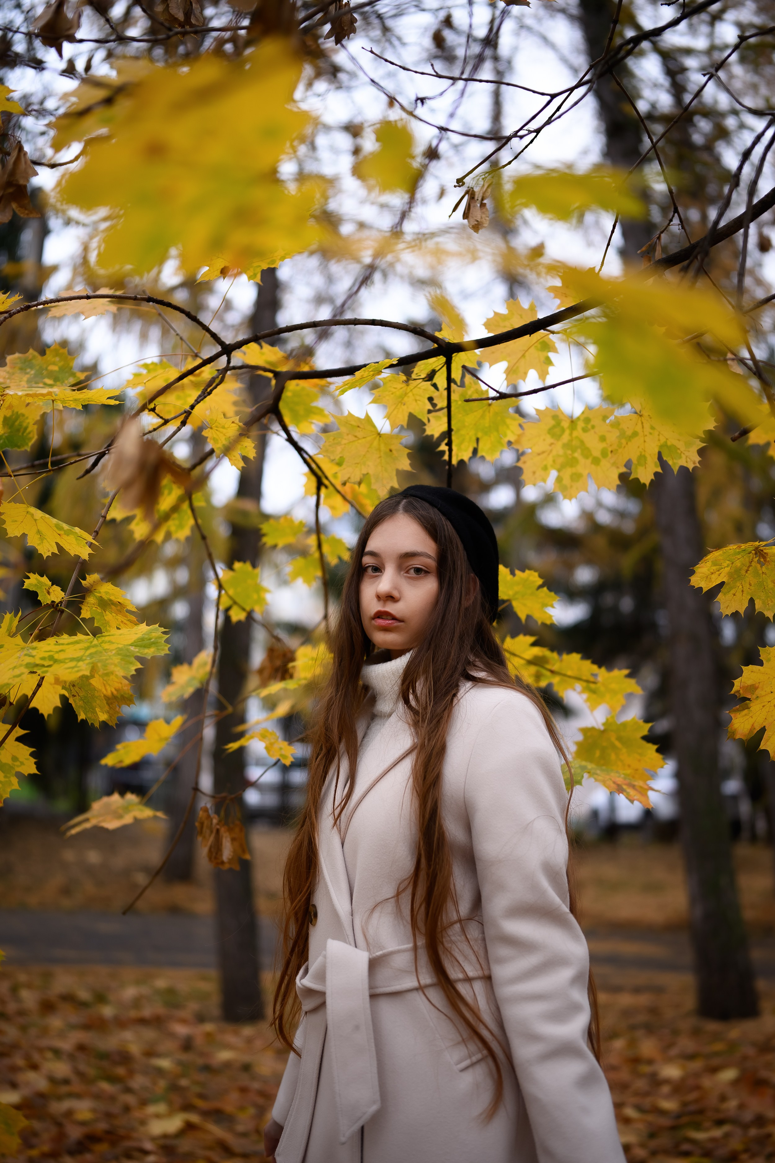 Девушка в светлом пальто позирует среди осенних деревьев в парке Казани