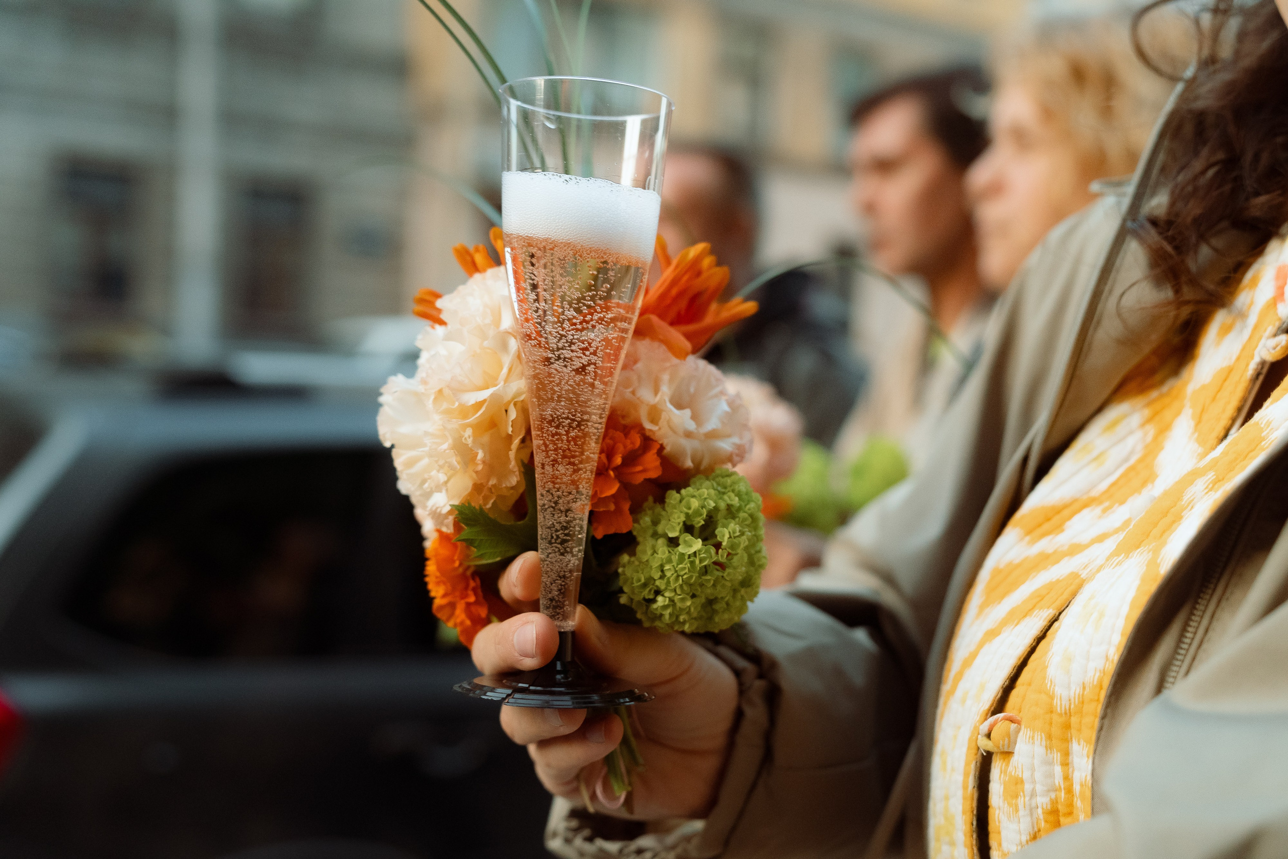 Гостья держит букет георгинов и бокал шампанского на тротуаре