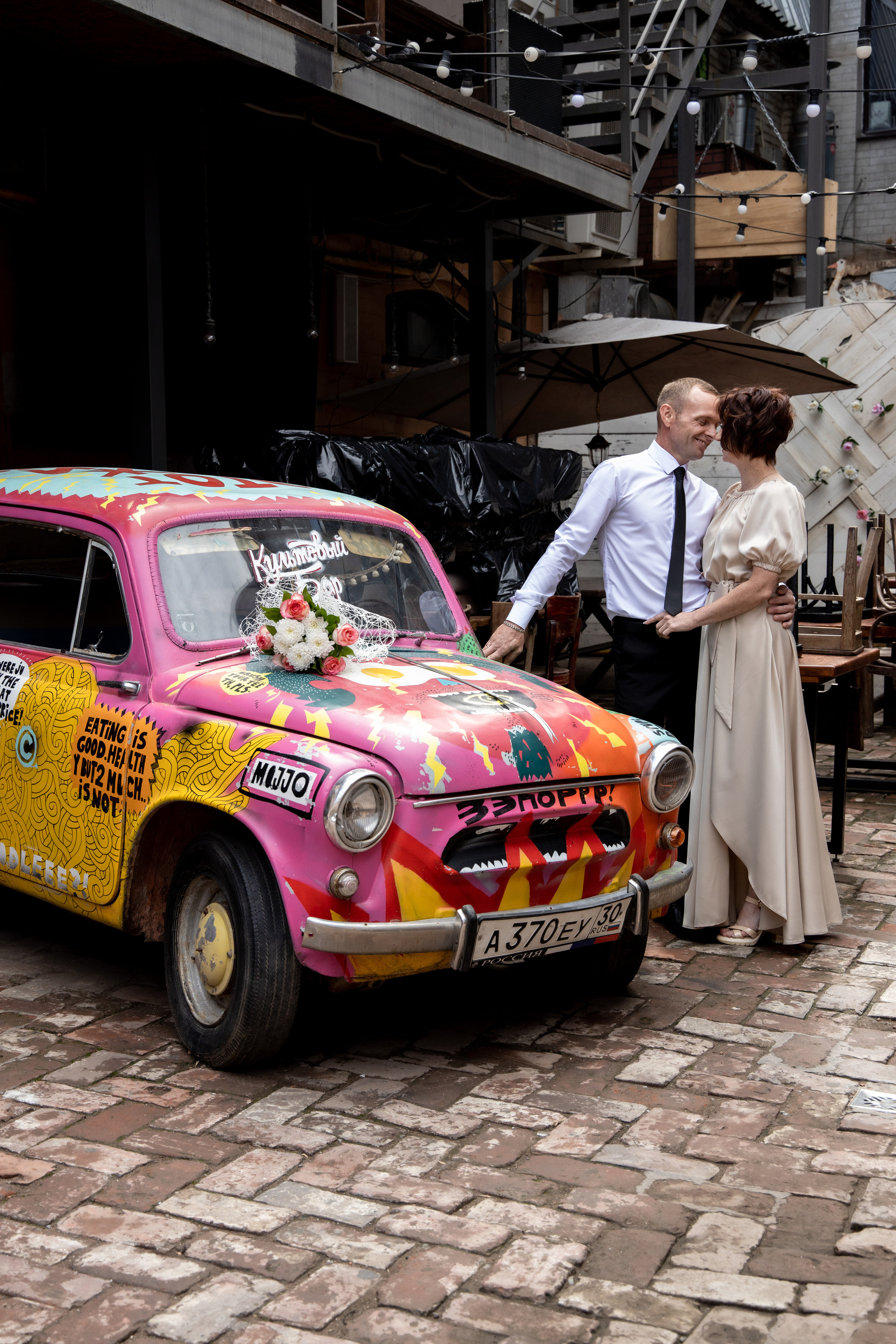 Жених и невеста на улице возле маленькой старой машины. Свадебная фотосессия Астрахань.