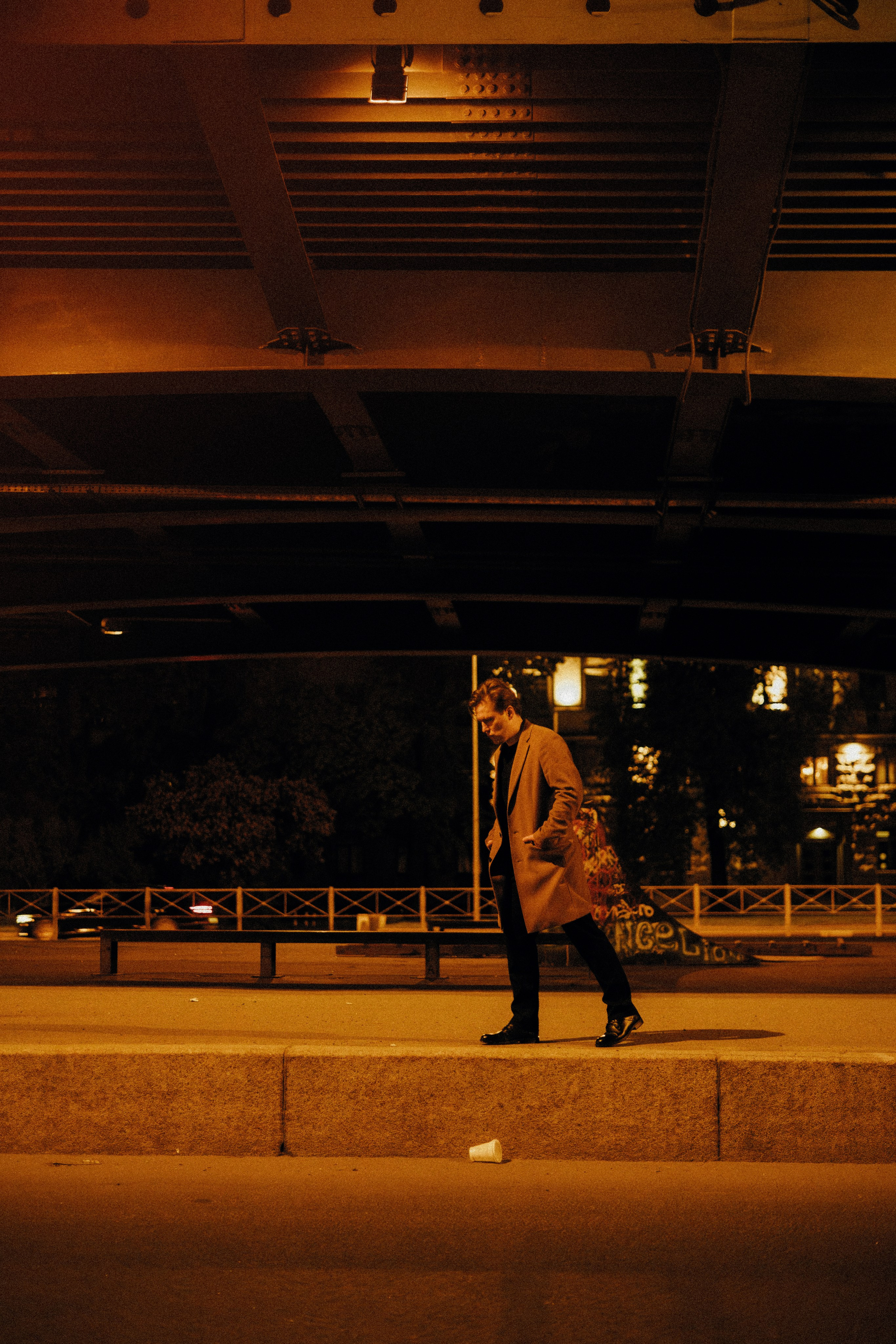 Молодой человек вечером один идет под мостом.