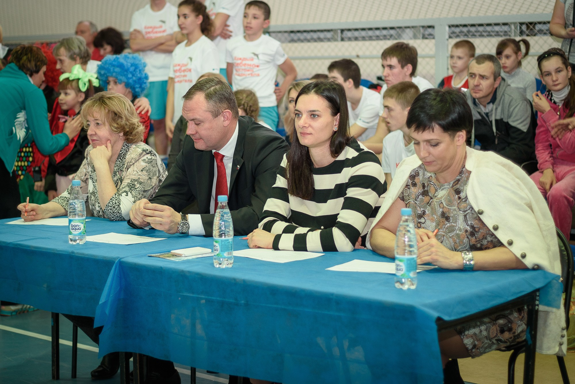 Елена Исинбаева в полосатом платье сиди за столом для судей соревнований